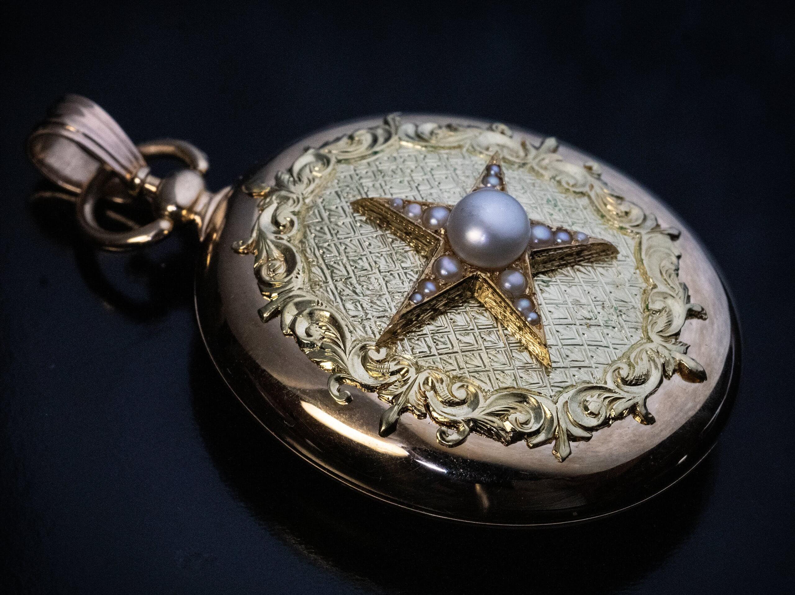 Austrian, circa 1870.  This large antique locket pendant is superbly crafted in two tone 14K gold. The front cover of the locket is centered with a pearl star mounted on an engraved background and framed by a hand-carved gold scrolling foliage. The