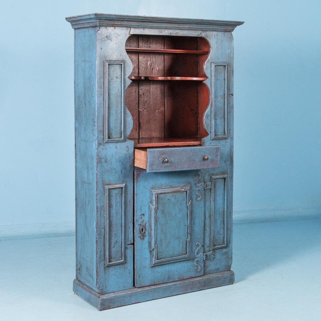 This antique country pine cabinet from Sweden is absolutely charming with remnants of old red paint showing through the blue outer coat where the paint is slightly distressed. The red paint inside the upper cabinet is a fun contrast to the blue,