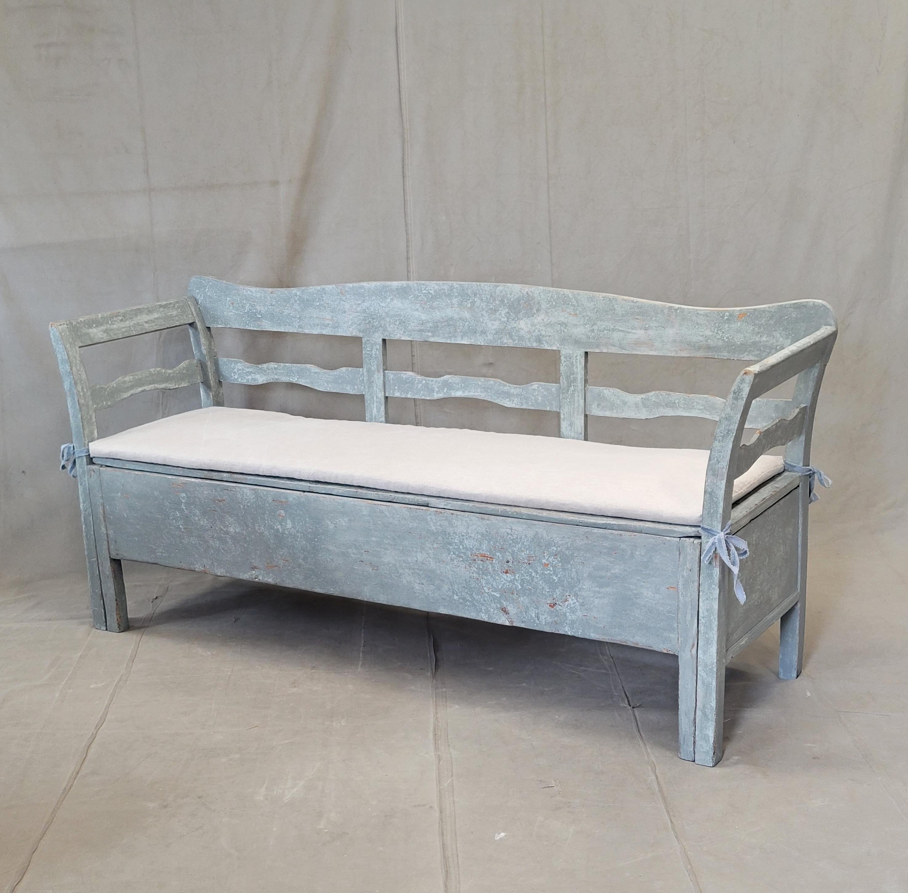 A beautiful antique late 1800s Swedish storage bench with distressed blue/gray paint and an optional custom made linen tie on cushion. This bench, also called a kitchen or trundle bench, was used to store bedding. At night the seat would be removed