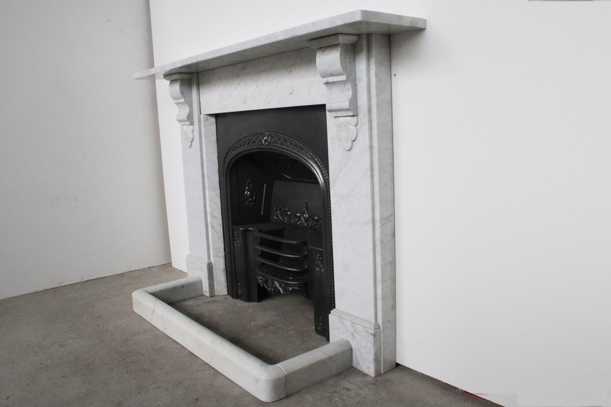 Antique 19th century Victorian Carrara marble fireplace surround with carved corbels supporting the shelf, and chamfered inside returns, circa 1870.
Pictured with an original Carrara marble fender and cast iron register grate, both priced