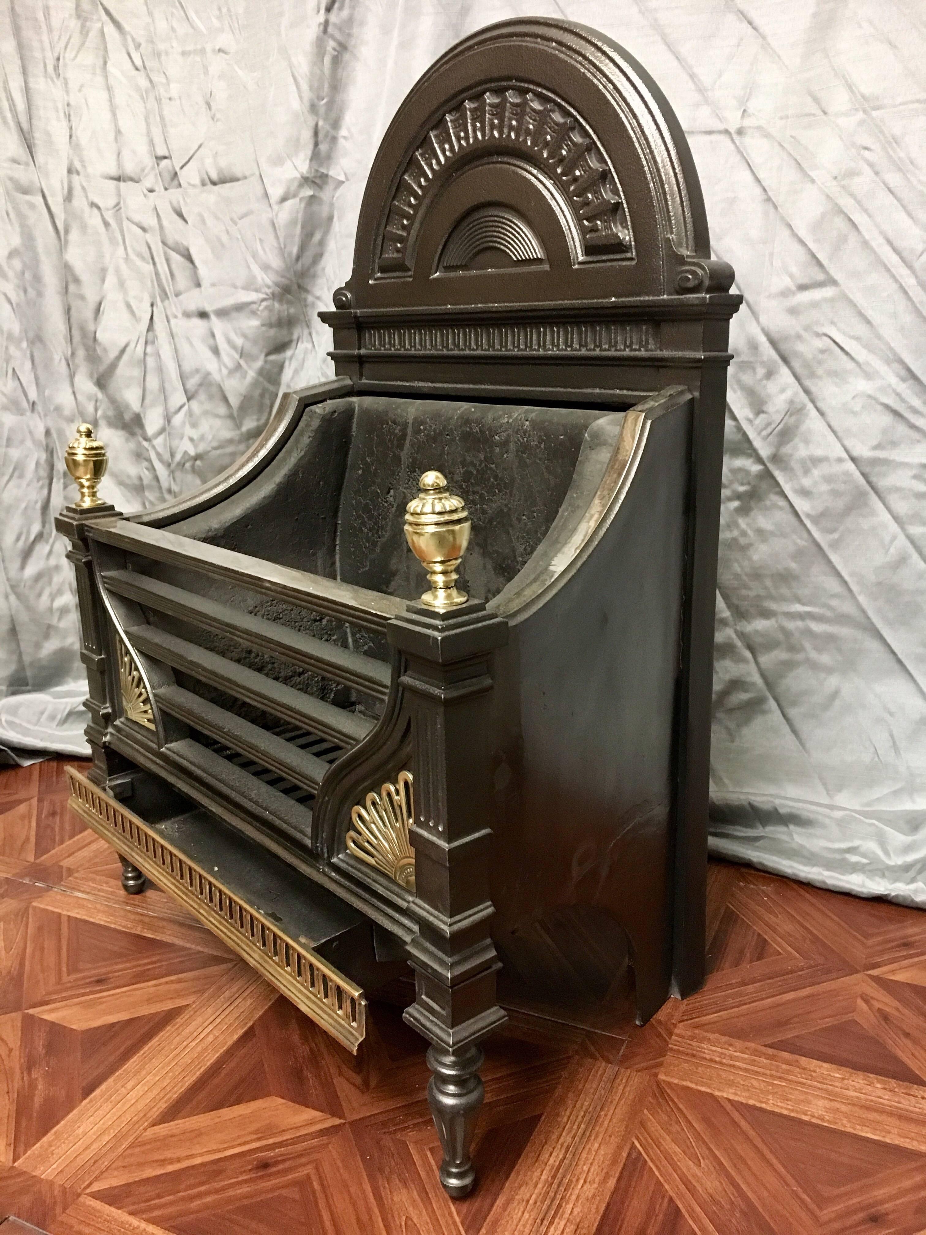 A fine antique Victorian cast iron and brass fire basket, a tall arch fireback encompassing a rainbow panel, supported by scalloped side panels connecting to a pillared four bar front, set with sunburst embellishments to each lower corner, capped