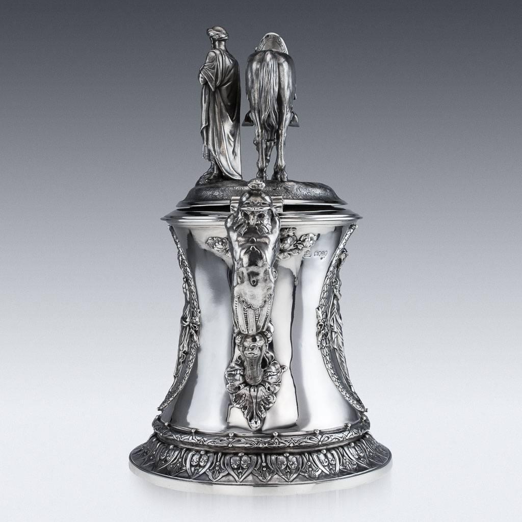 Antique 19th century monumental Victorian solid silver flagon of waisted cylindrical form with a mythological Kraken mask spout and male term monopedia handle, the sides decorated with wreathed panels of winged classical nudes, the hinged cover