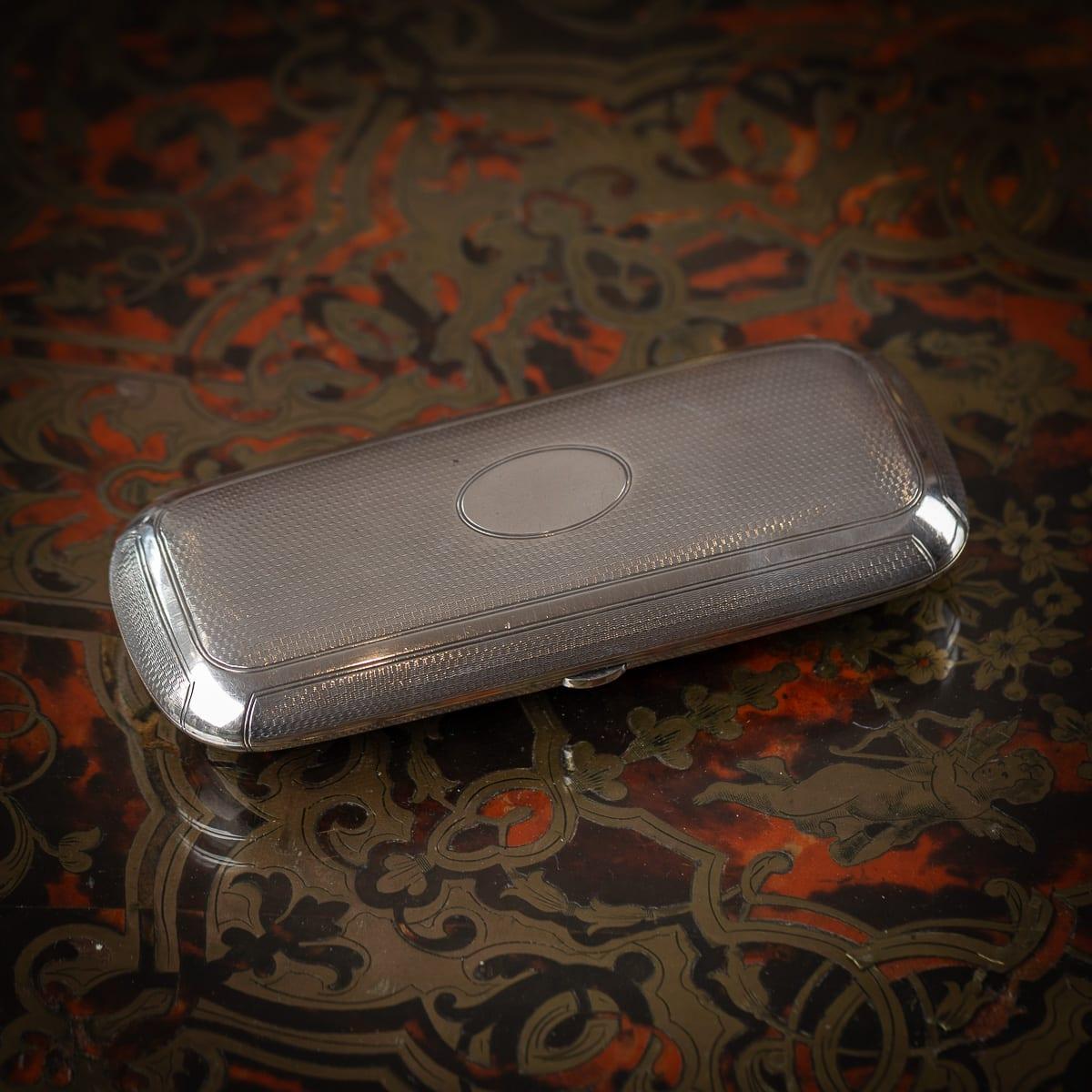 Antico portasigari in argento massiccio inglese del XIX secolo. Rettangolare con bordi arrotondati, la cassa è decorata con un motivo a motore e presenta un cartiglio centrale vuoto. L'interno è riccamente dorato e dotato di un fermaglio a molla