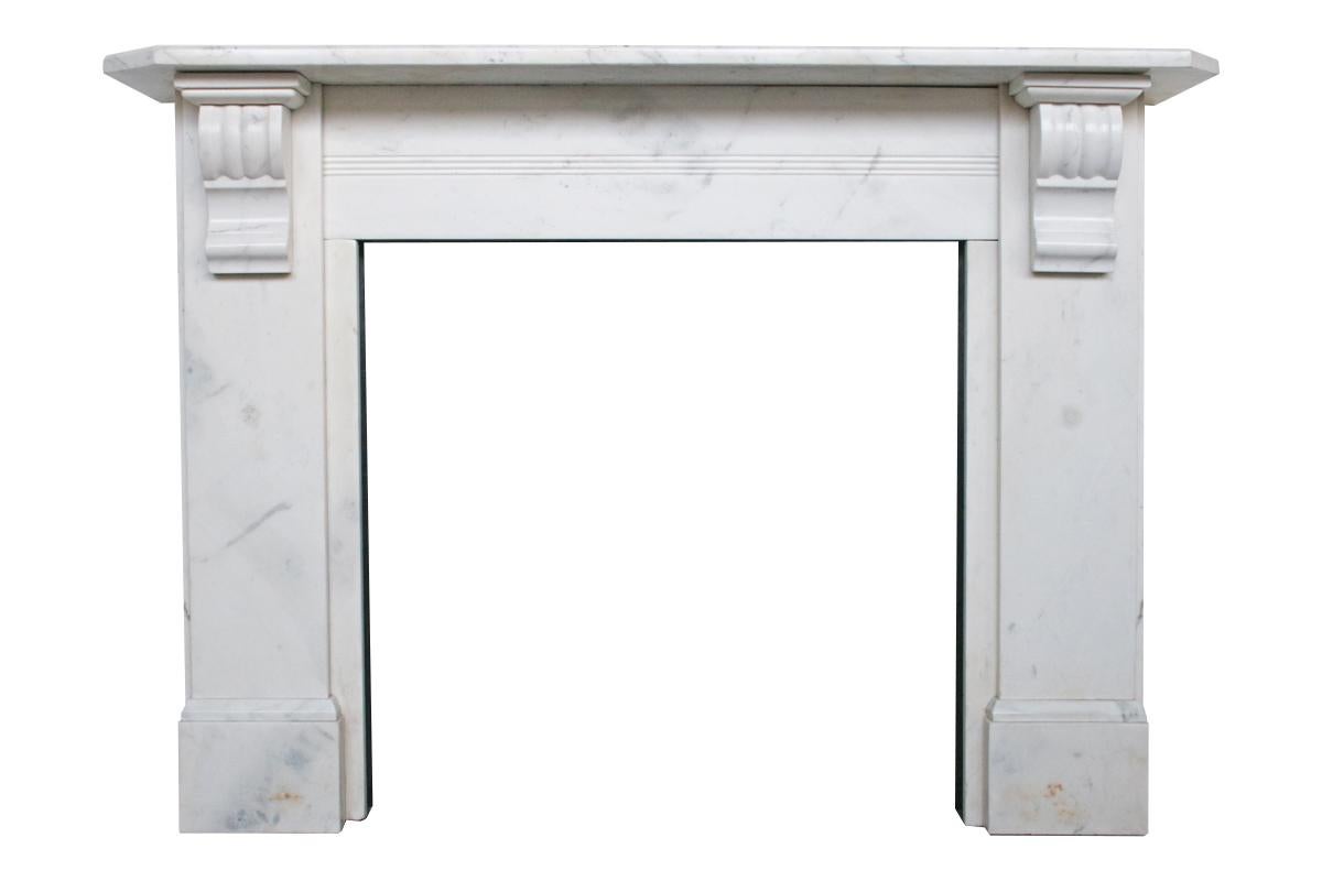 Antique 19th century Victorian white marble fireplace surround with carved corbels supporting the shelf with chamfered corners and edge and reeded detail to the frieze, circa 1860.
Pictured with an original cast iron arched grate, sold