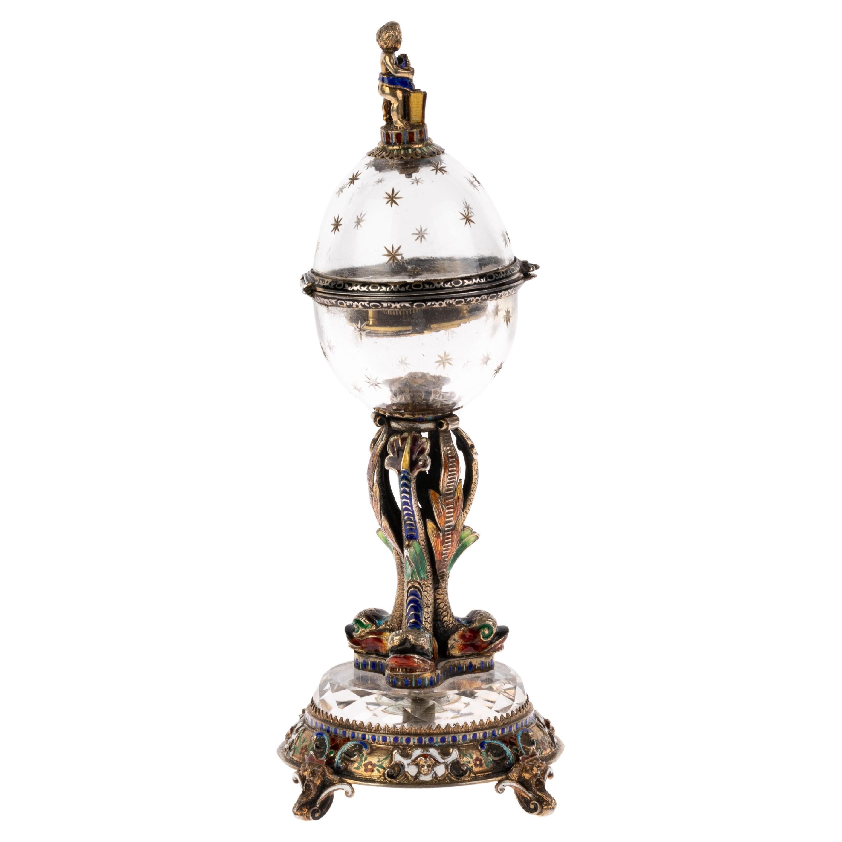 Antique 19th Century Viennese Austrian Enamel & Silver Rock Crystal Desk Clock by Hermann Böhm. Vienna, c.1880, the egg-shaped case surmounted by the figure of a putto, opening to reveal a brightly enamelled circular dial and bright enamel borders,