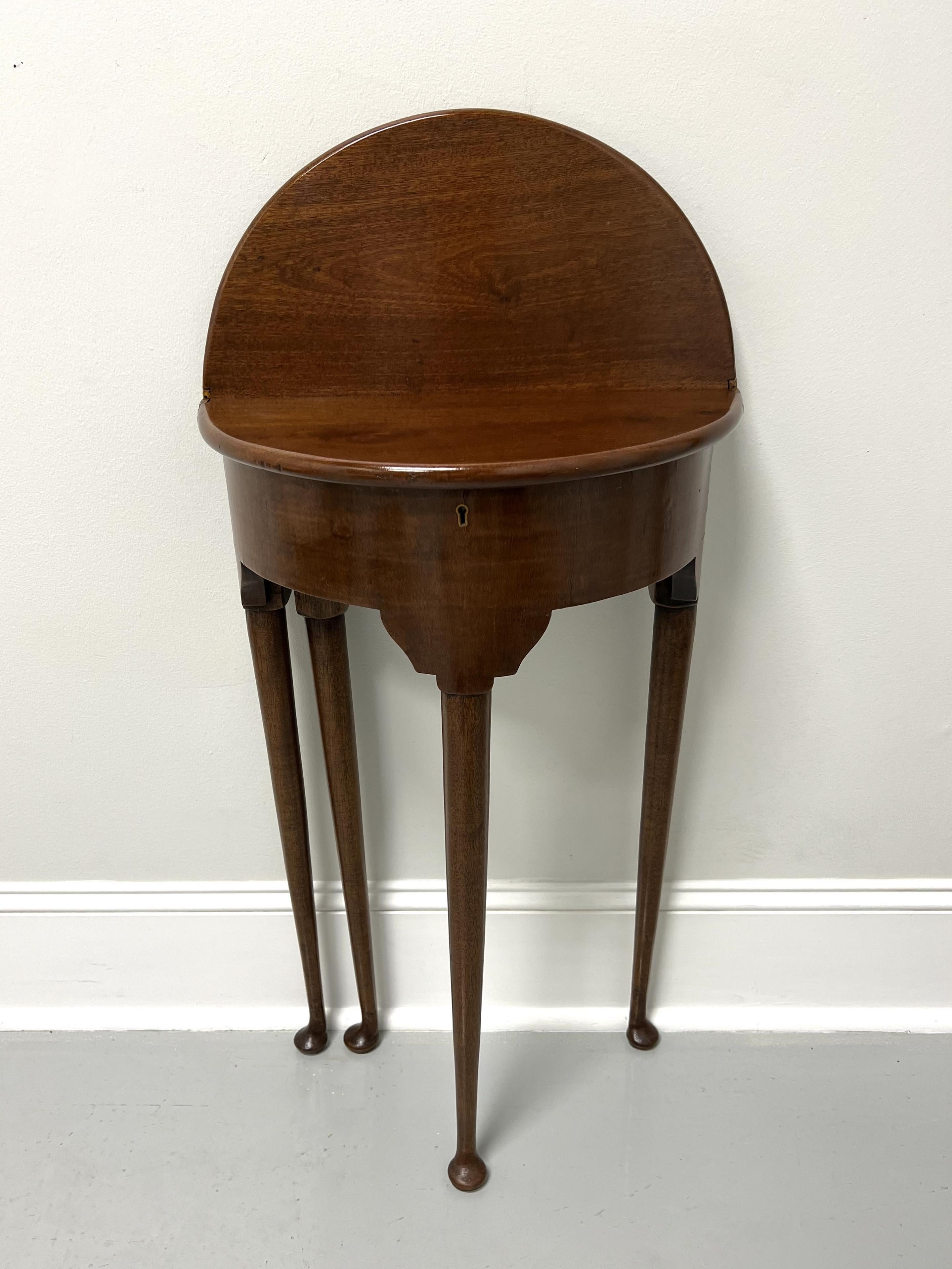 An antique 19th Century Georgian style petite flip top demilune table. Solid walnut, brass hinge hardware, half moon shape, flip top with smooth rounded edge, smooth apron carved at top of legs, tapered round straight legs, and pad feet. Back