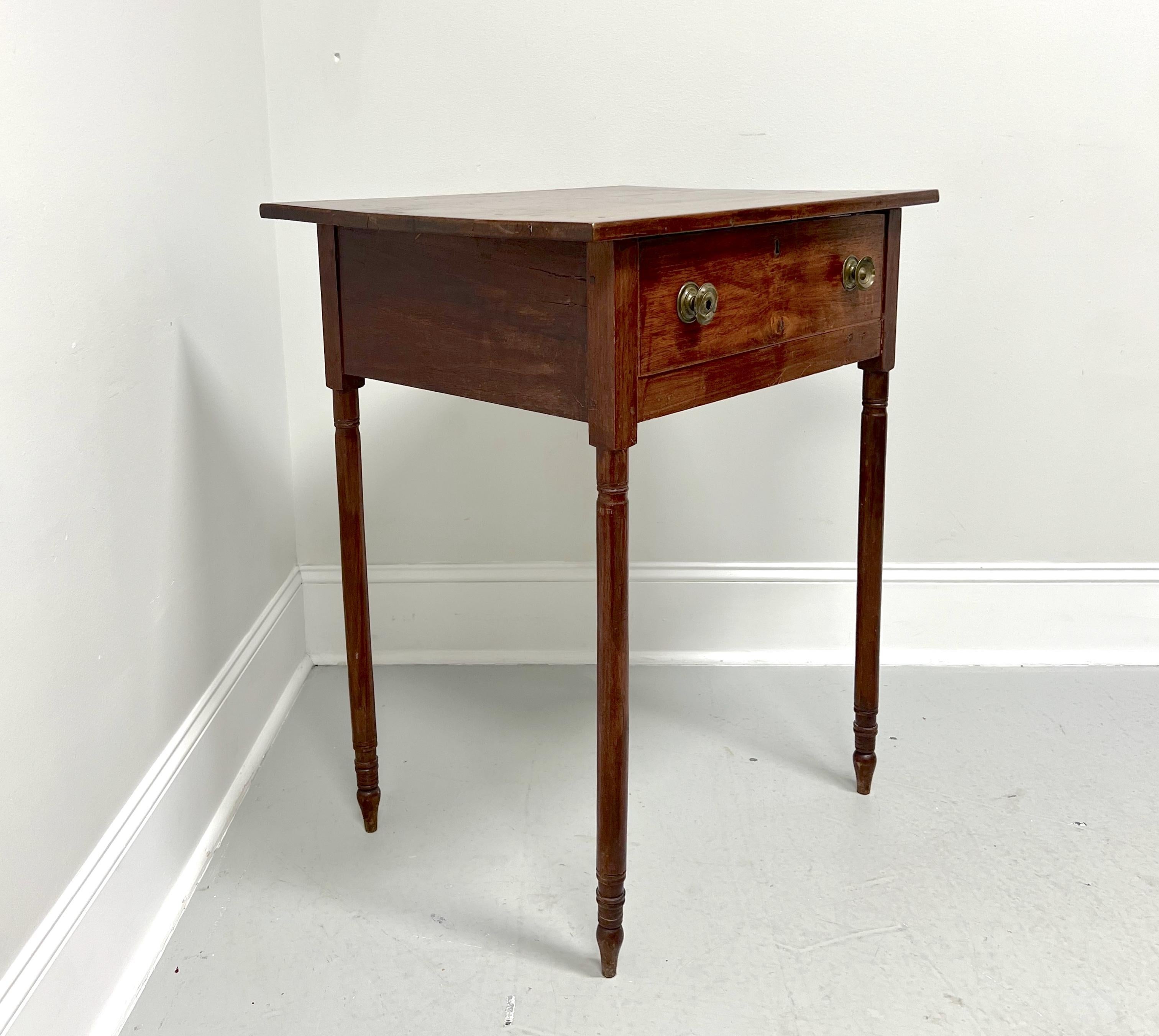 An antique 19th Century rustic side table, unbranded. Handcrafted of walnut, naturally distressed from age, squared edge to top, brass hardware, and turned straight legs. Features one lockable drawer of rabbet joint construction. Likely made in the