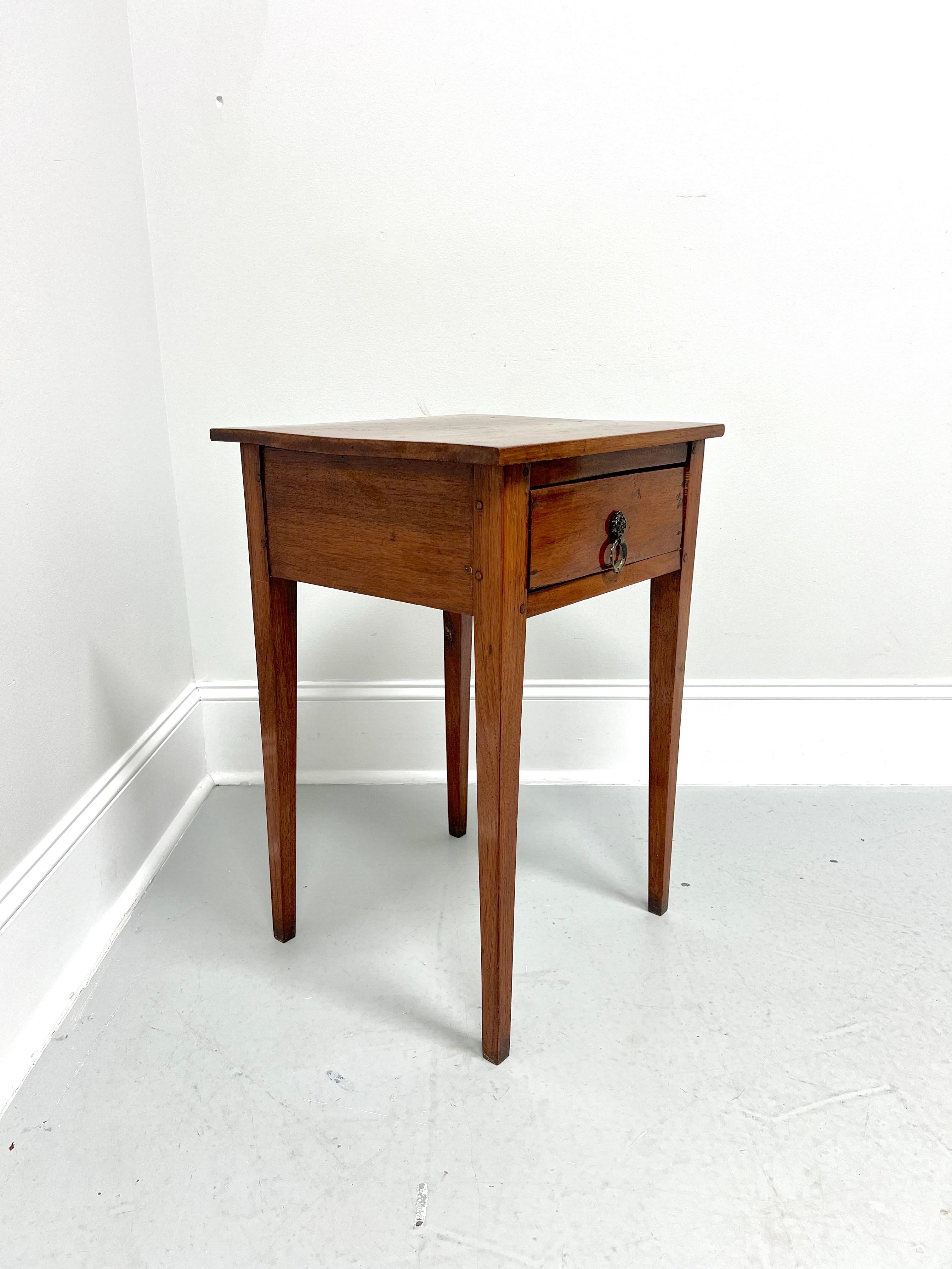 An antique 19th Century rustic side table, unbranded. Handcrafted of walnut, naturally distressed from age, squared edge to top, brass pull hardware, and tapered straight legs. Features one drawer of rabbet joint construction. Likely made in the