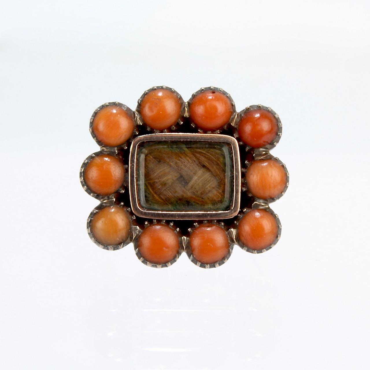 A wonderful, diminutive Georgian or early Victorian gold-filled and woven hair brooch or pin.

With braided hair behind glass set in a gold-filled setting surrounded by small pink coral cabochons. 

In the Georgian and Victorian eras, woven hair art