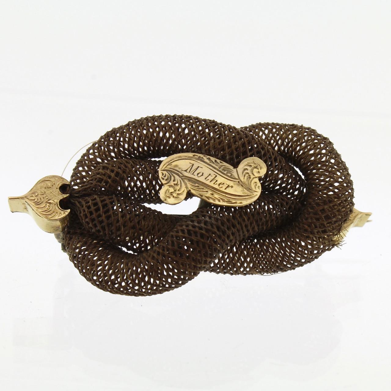 A good late Georgian or Victorian memorial hair art brooch.

Comprised of an interlocking double looped knot of woven hair mounted with a central scroll-shaped cartouche engraved with the dedication that reads 