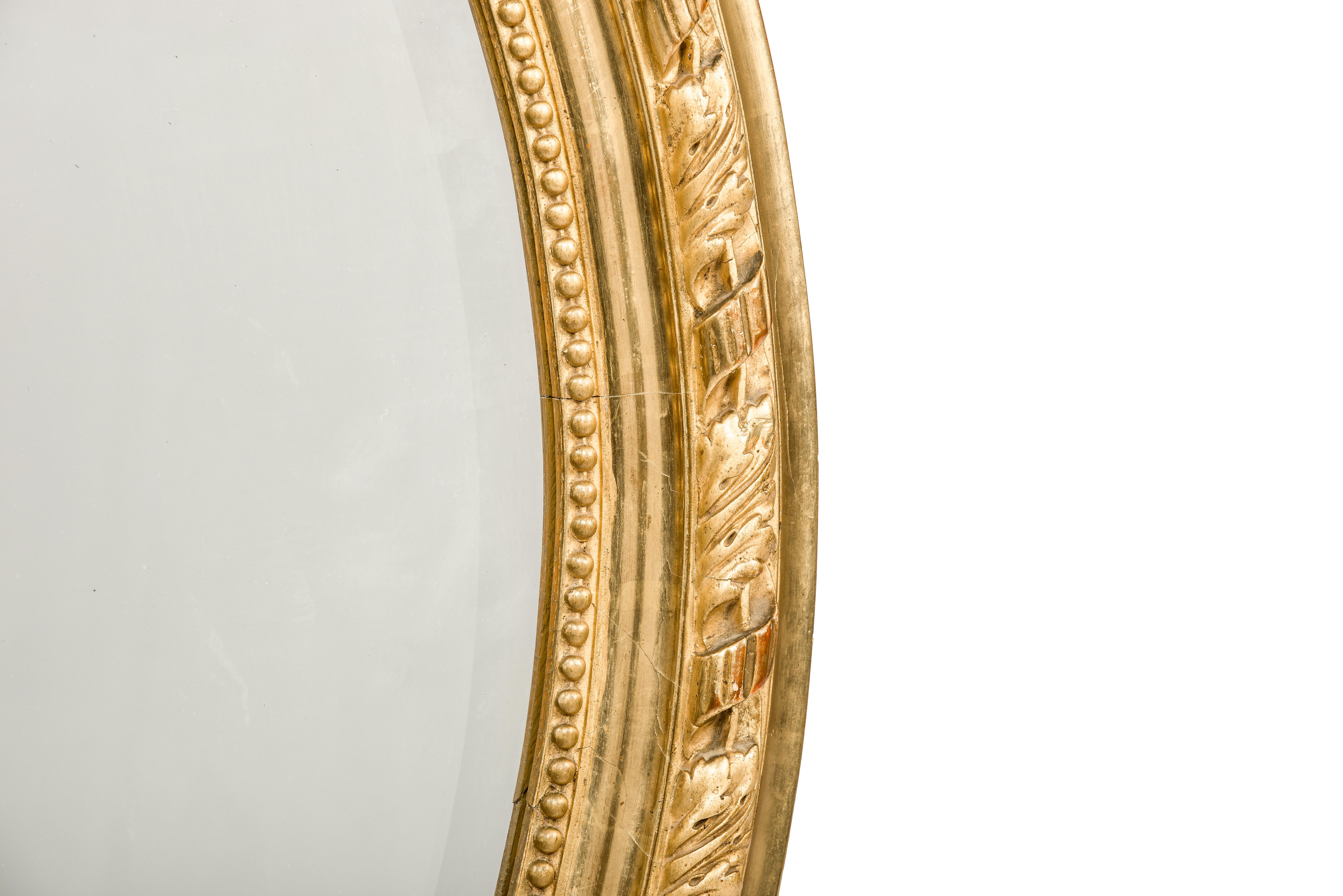 Nous vous proposons ici un magnifique miroir ovale antique doré à la feuille d'or qui a été fabriqué en France à la fin du 19e siècle. Le miroir a un cadre ovale en pin massif, lissé au gesso et décoré d'ornements. Le cimier supérieur présente une