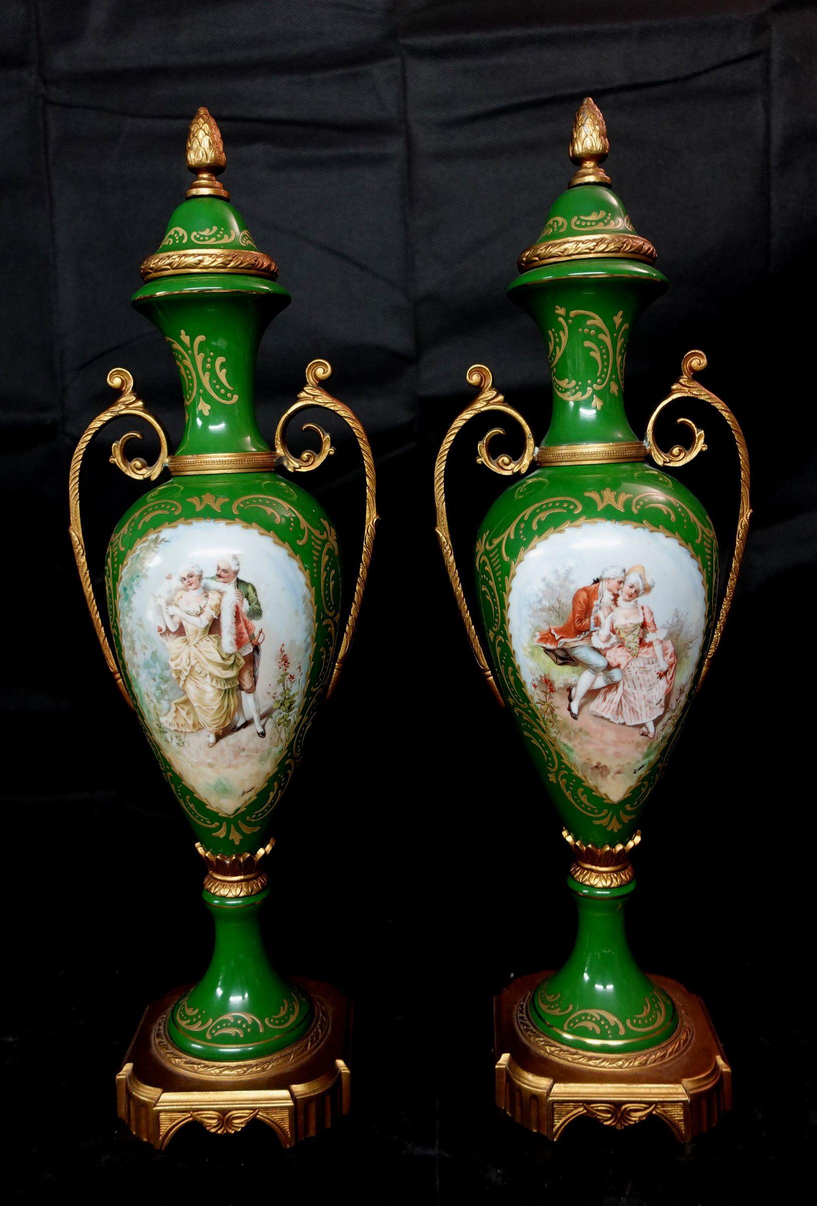 Antique a pair of matching green bolted urns with amorous scenes and with gilt metal mounts and gilt highlights. Beautiful hand-painted royal figures at the centers of both vases, made in Czechoslovakia.



