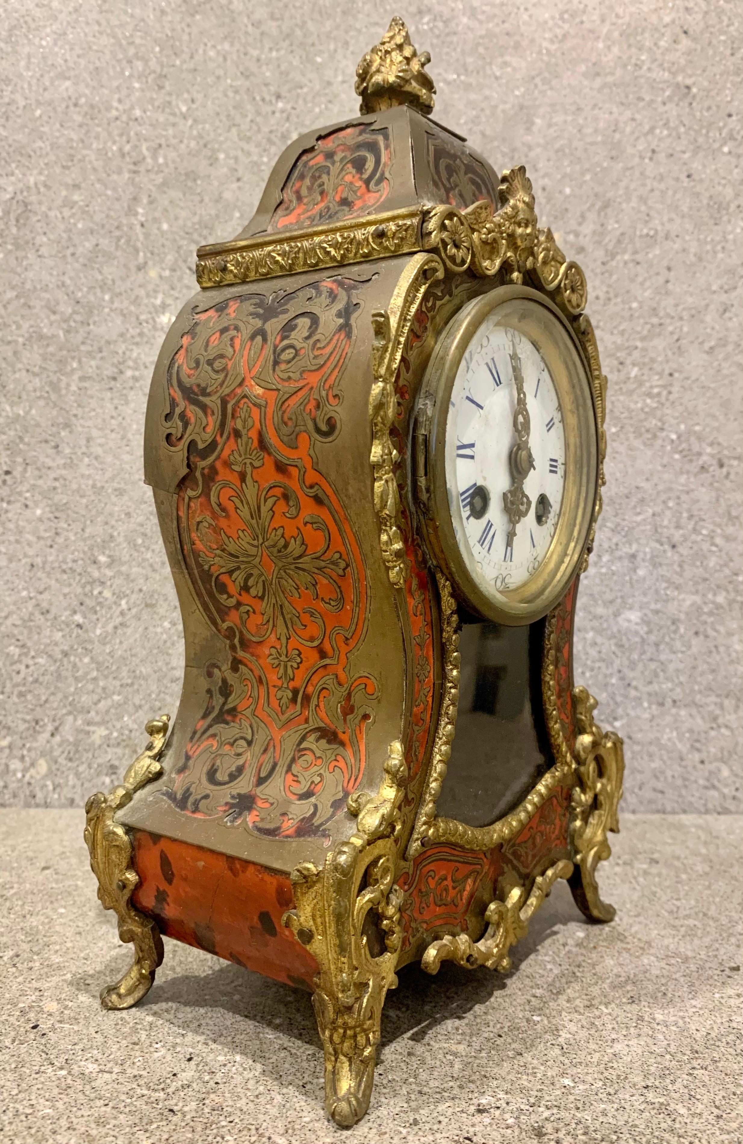 A superb quality French boulle tortoishell mantel clock. Red ground with fretted brass boulle inlay. The front glazed panel with a visible Louis IV pendulum. Gilt bronze case mounts and surmounted by a finial. white porcelain dial. An 8-day duration