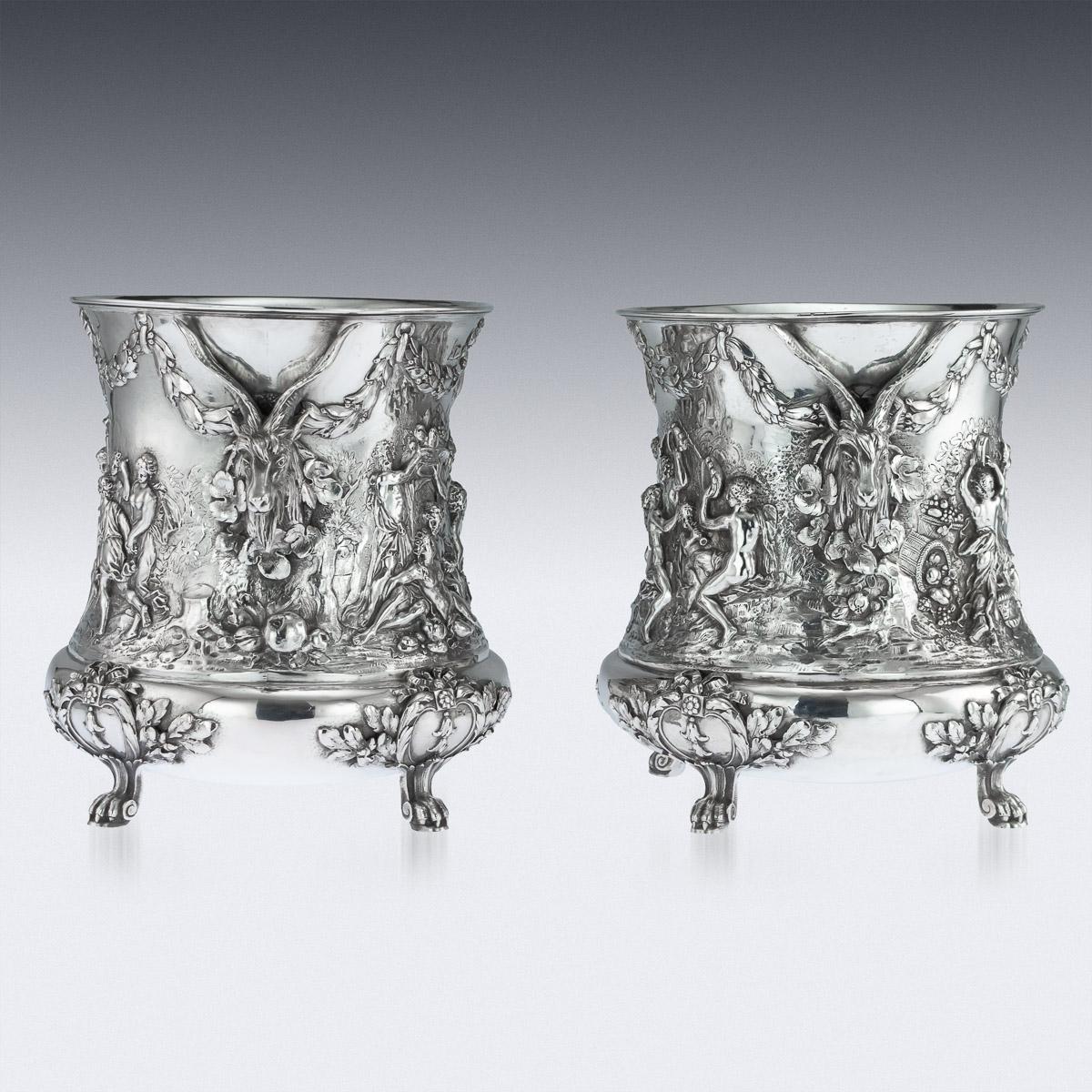 Antique late-19th century German pair of solid silver wine coolers, each exceptionally decorative and ornamental, of vase form on four paw feet, the sides embossed and chased in high relief with classical bacchanalian scenes, depicting figures and