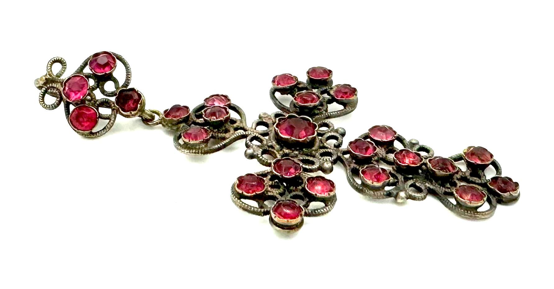 Ces croix étaient portées dans le nord de la France, en Normandie. 
Cette croix a été fabriquée à la main dans le deuxième quart du XIXe siècle en fil de fer forgé et en laiton. La croix est sertie d'une grande pierre en pâte rose au centre de la