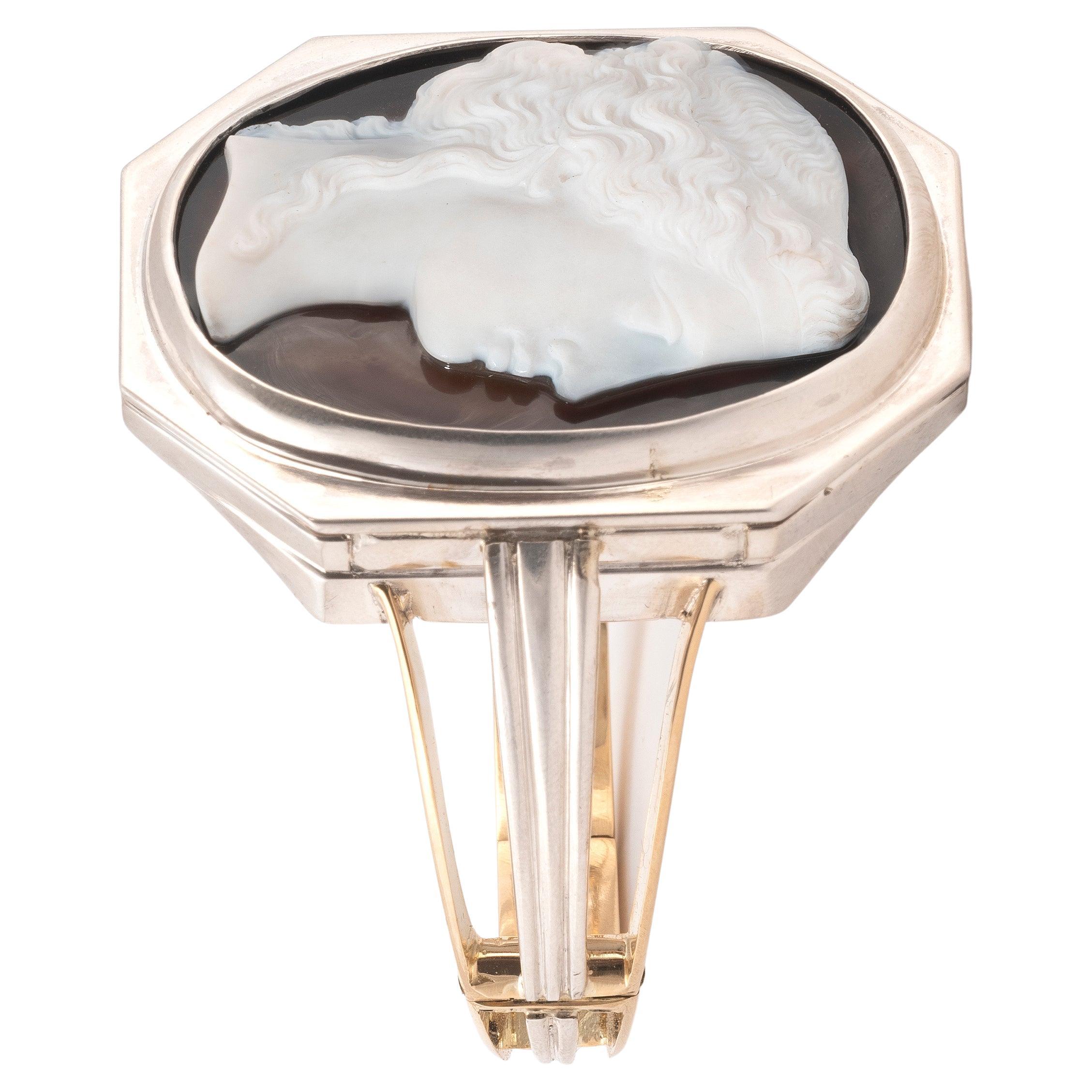 The oval cameo carved of white and black agate to depict a young maiden in three-quarters profile, with fine detailing to the flowing hair, jewelry and Empire style dress, bezel-set in 18K yellow gold and silver, hinged bangle, inner circumference