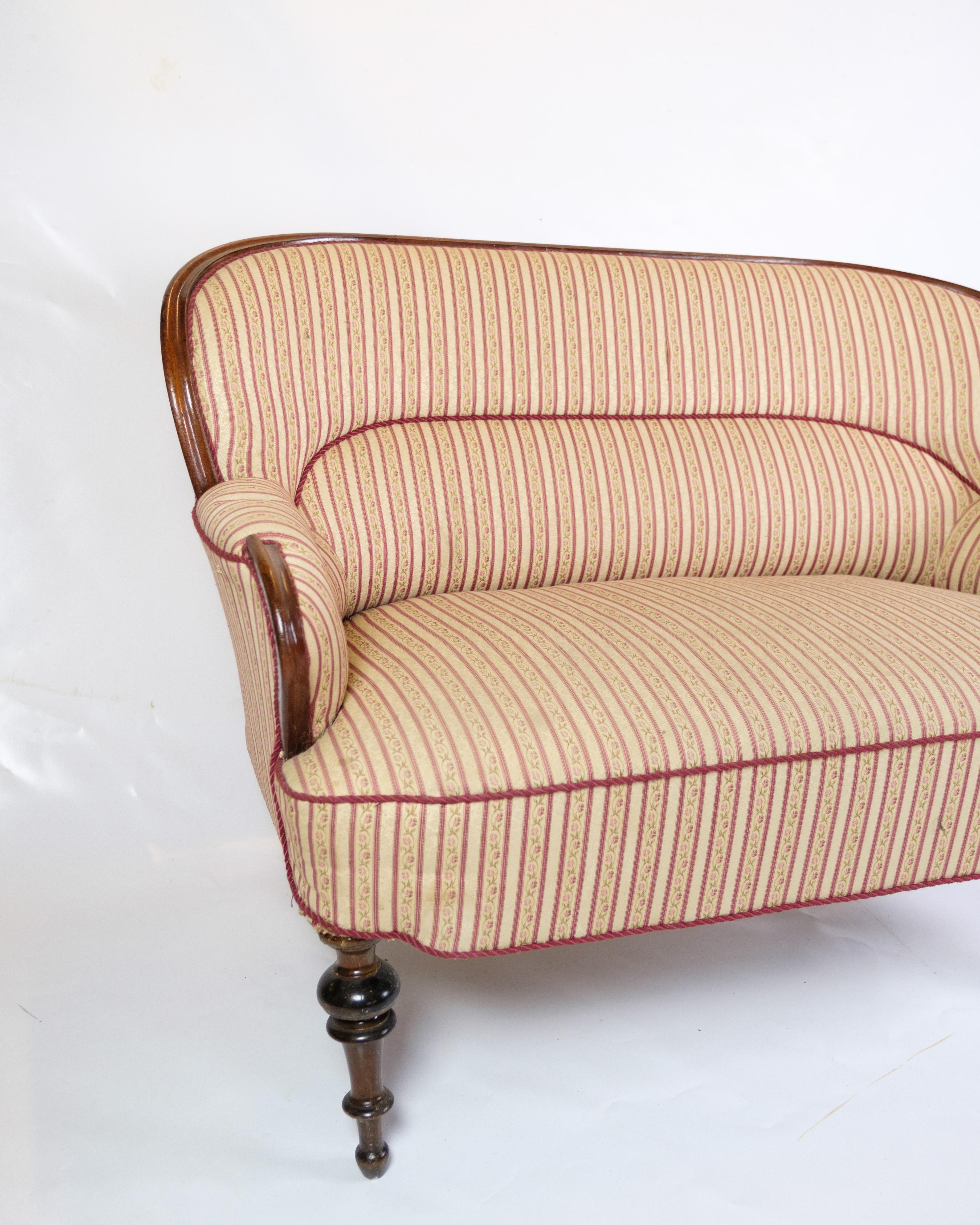 Ce canapé ancien à deux places, datant d'environ 1890, est un bel exemple d'artisanat et d'élégance d'époque. Fabriqué en bois d'acajou, le canapé dégage un charme intemporel et une grande durabilité. Tapissé d'un tissu aux motifs magnifiques, il