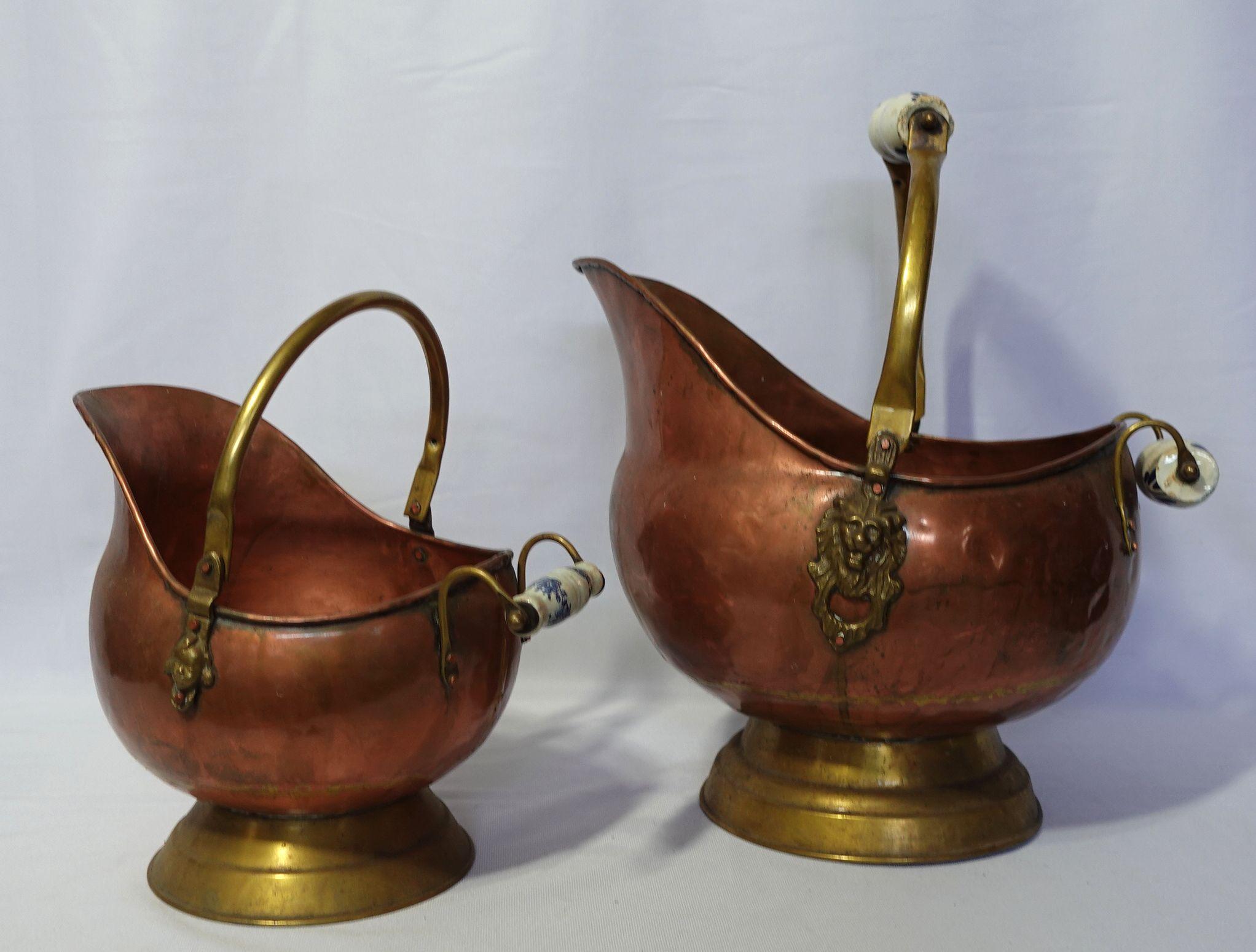 Antique 2 Hand Hammered copper coal scuttles with blue and white ceramic handles and brass lion head accents in the large one, and the medium one with a girl's head.
Large: 15” from handle to spout. 12” wide and 16” tall with the handle up. Some