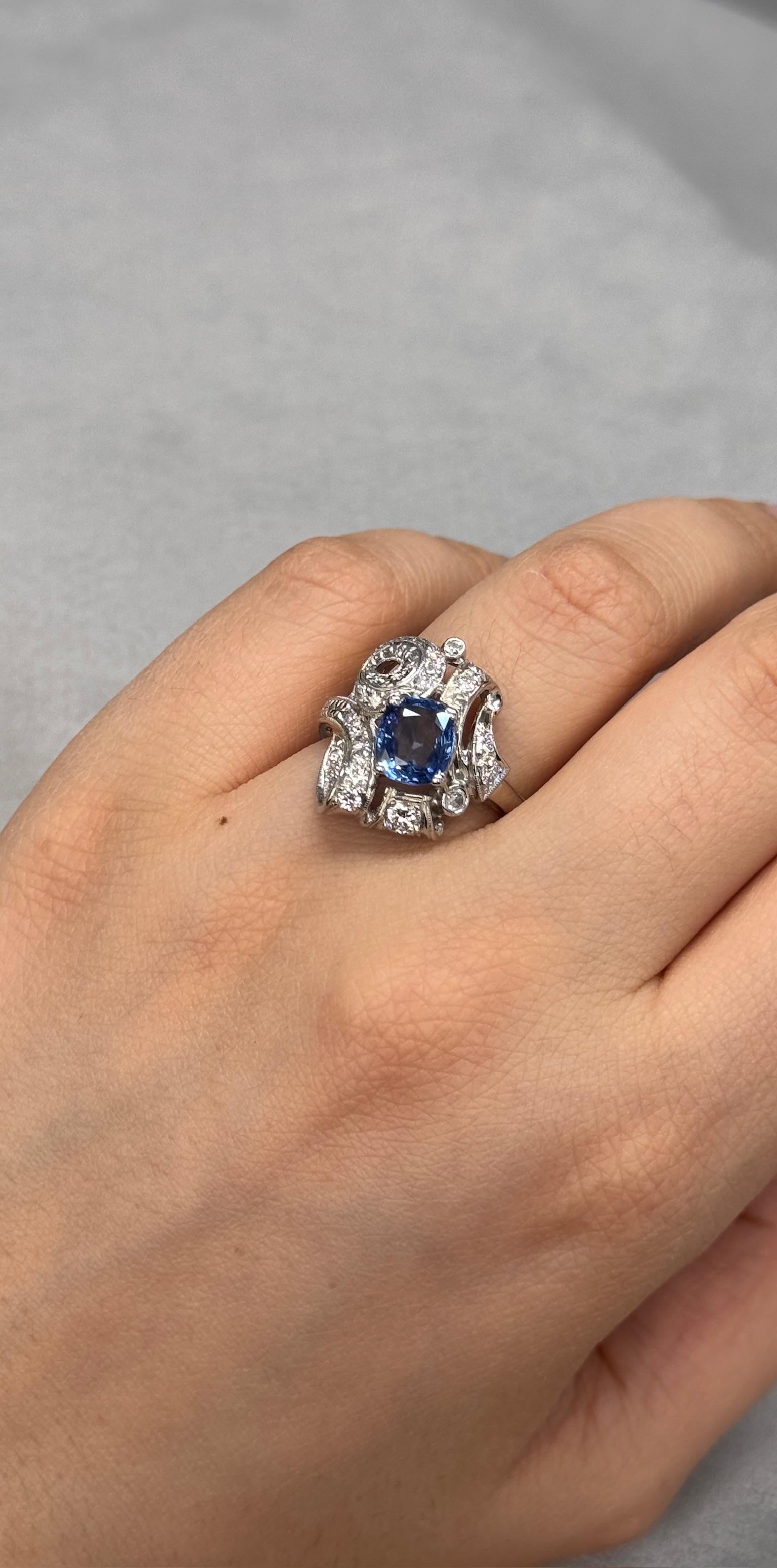 Véritable trésor vintage, cette bague ancienne est ornée d'un saphir naturel chauffé du Sri Lanka d'une taille coussin de 2,08 carats, d'un bleu profond et brillant. Encadrée par 20 éblouissants diamants d'accentuation totalisant 0,70ct, le plus