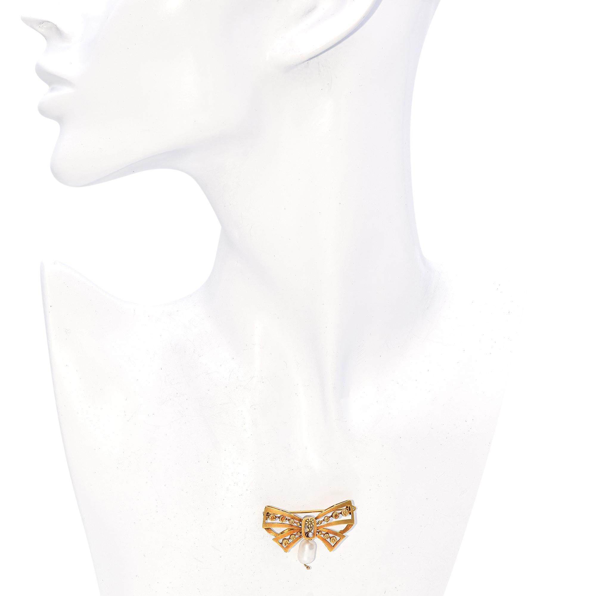 This exquisite piece is crafted in 20k gold, forming an elegant bow motif with intricate openwork design. Adorning the bow are delicate floral embellishments, each meticulously detailed. At the center, a small pearl is nestled within a floral