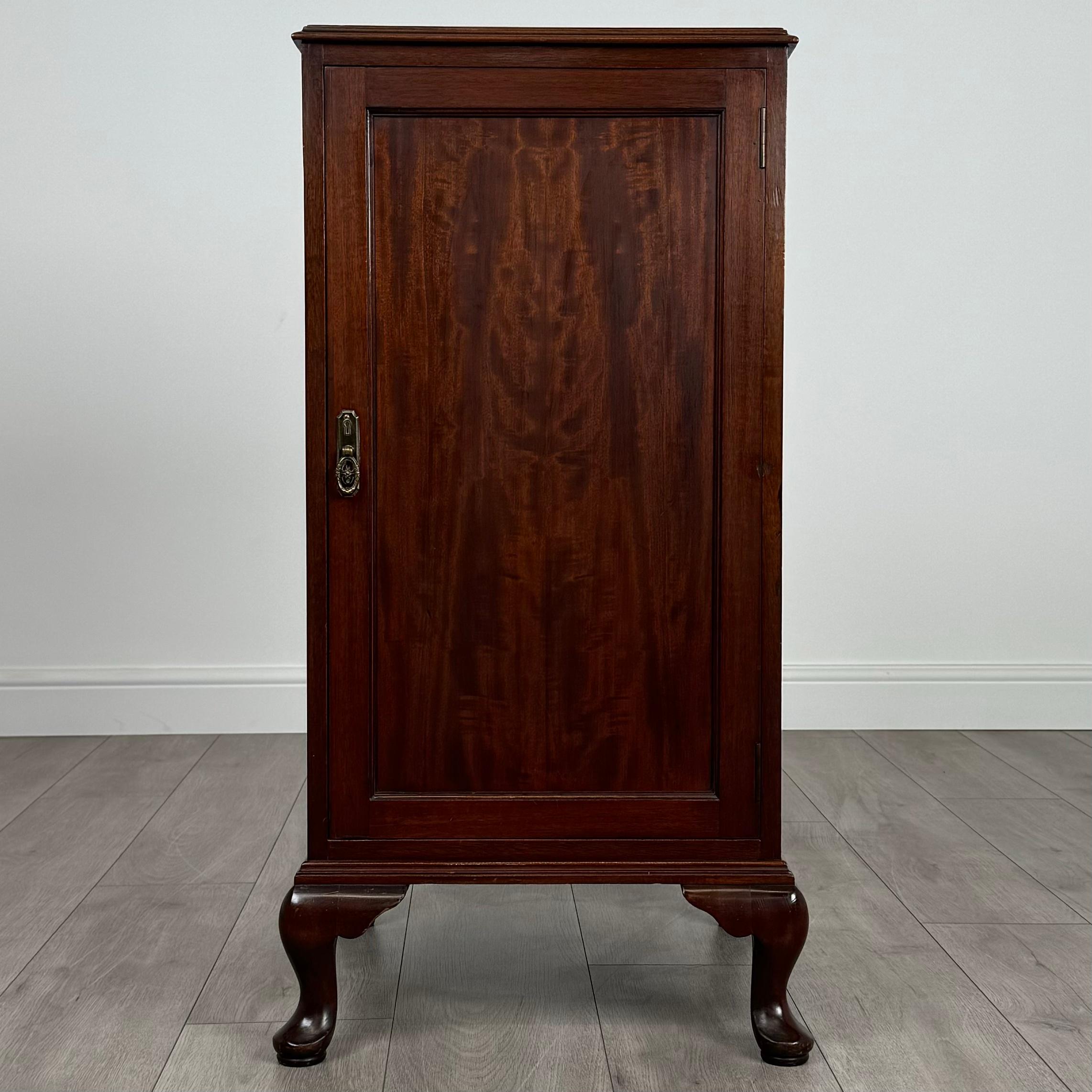 Cette élégante armoire de style Queen Anne du XXe siècle, fabriquée en acajou fin, est une pièce magnifiquement conçue qui respire la sophistication intemporelle. 
Reposant gracieusement sur de petits pieds cabriole, il incarne les courbes raffinées