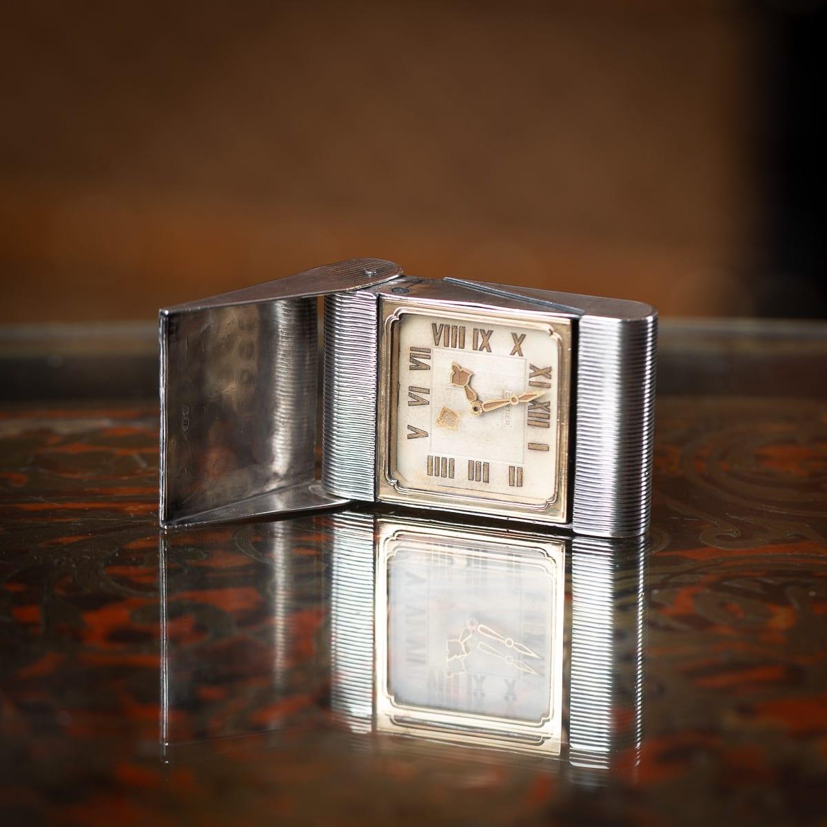 Antique 20th Century French solid silver Cartier travel clock, elegantly crafted with an engine turned outer case. When opened, it reveals a square-faced travel clock, the dial marked 'Cartier' with Roman numeral hour markers. Hallmarked with