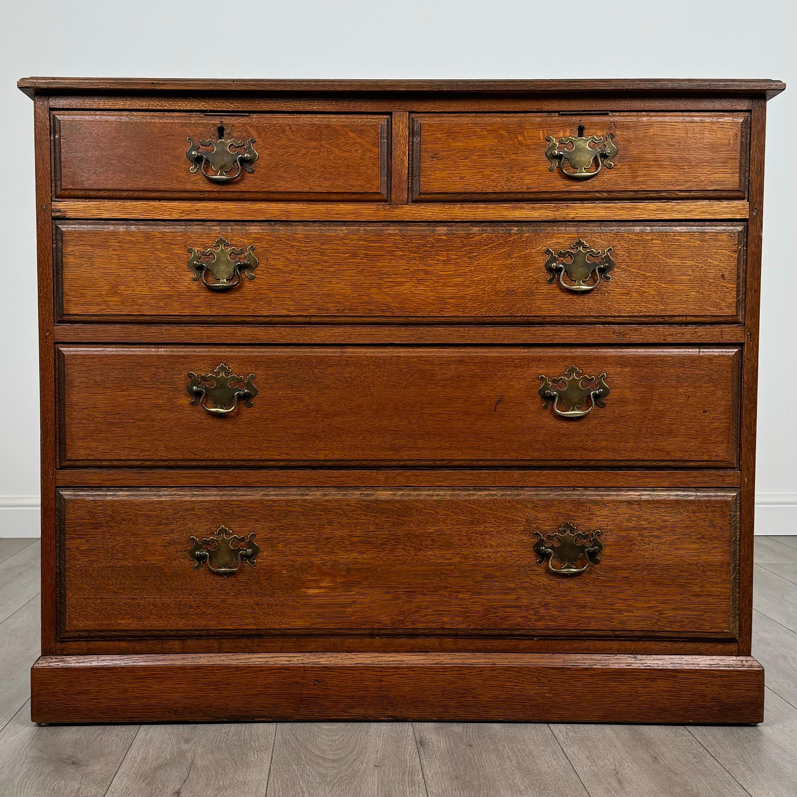 This antique 20th-century chest of drawers, crafted from solid oak, is a piece of excellent quality with a timeless and practical design. 
Standing on a sturdy plinth base, it offers both durability and elegance, making it a versatile addition to