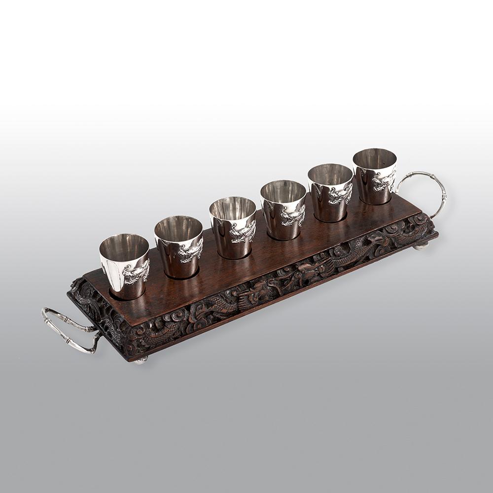 An exquisite and unusual antique Chinese solid silver liquor set, with six beautifully applied beakers with dragon design, sitting within its original rectangular rosewood Stand, carved with Chinese characters and dragons, and sides mounted with