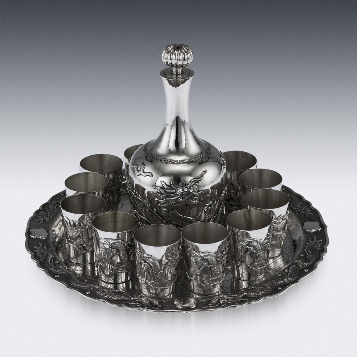 Antique early 20th century Chinese solid silver sake drinking set, comprising of a lidded bottle, twelve beakers and a tray. Each piece is very decorative, bottle applied with a flying dragons and mounted with a removable stopper, the beakers are