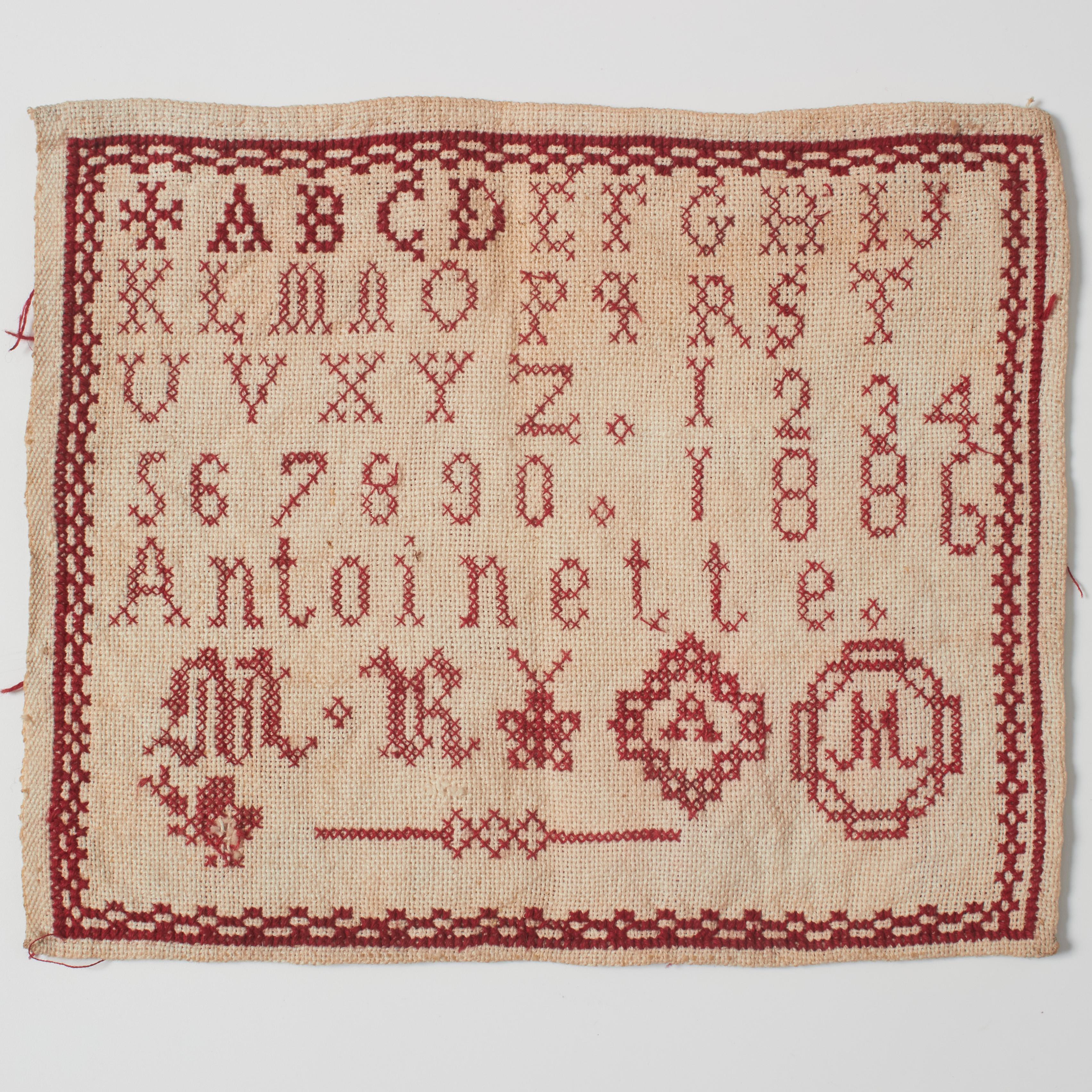 Embark on a journey through time with our antique cross-stitch sampler from the early 20th century. This captivating piece features a rich crimson-on-ivory design, showcasing finely crafted letters of the alphabet, numerals, and an ornate border