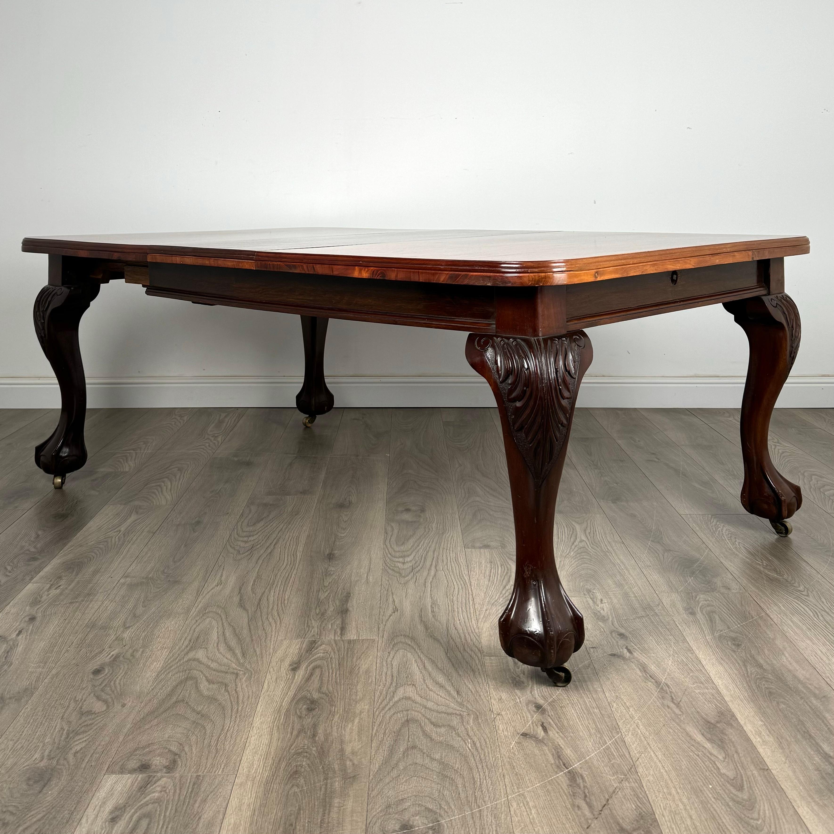 Magnifique table de salle à manger du 20e siècle en acajou, avec des pieds décoratifs en cabriole, des pieds en griffe et en boule et des roulettes en laiton. Cette pièce élégante comprend une feuille supplémentaire et une poignée enroulable, ce qui