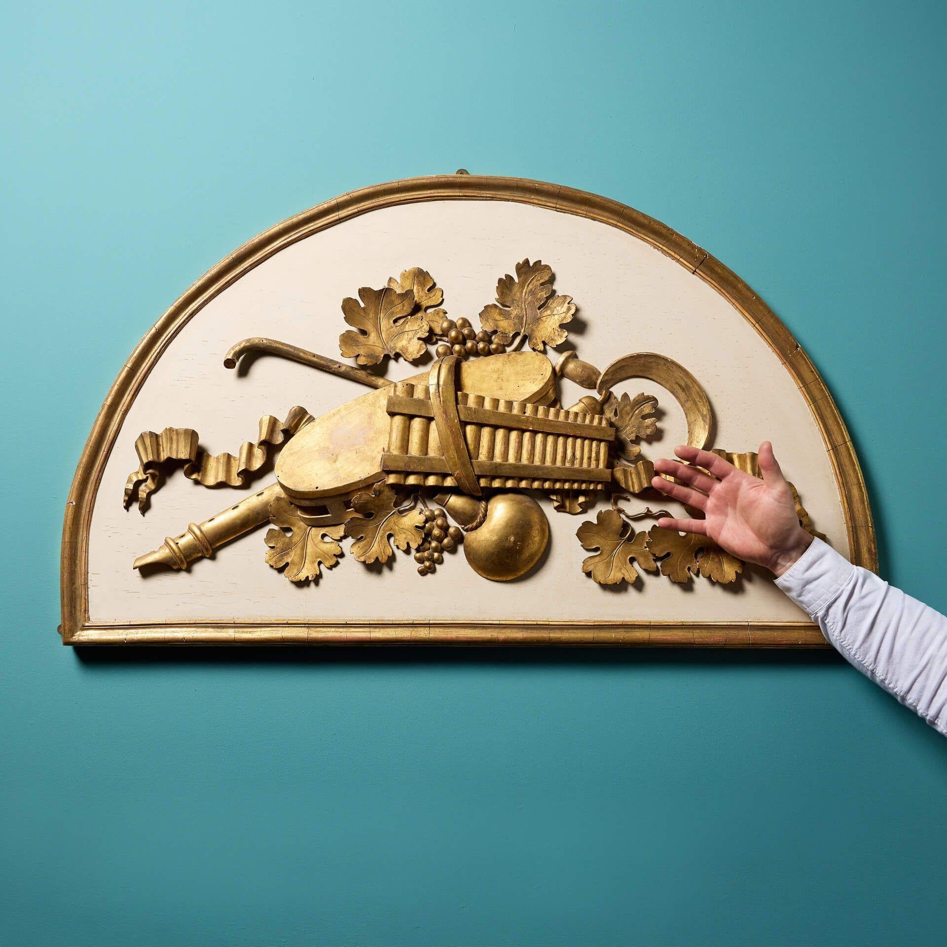 An antique 20th century domed wall panel.

The intricate design of the carved lime wood features carved fruits and musical instruments to a pale background with beautiful gilded decoration.

The good scale and hanging hooks only add to this charming