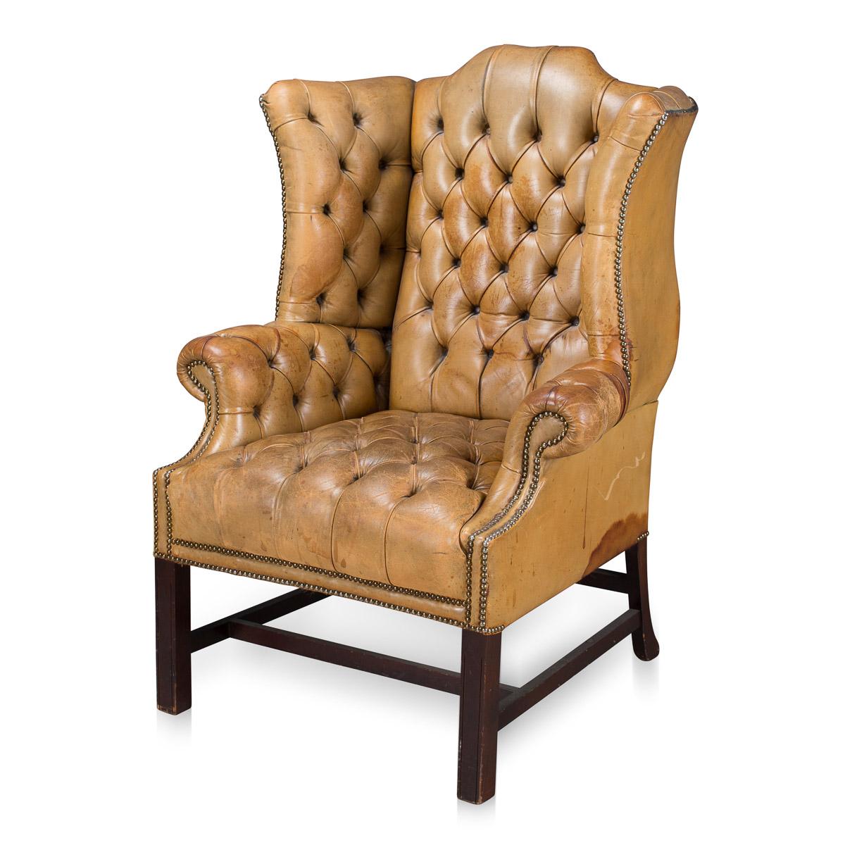 Antique early 20th century truly stunning example of English leather craftsmanship, this leather wing-back armchair has an exceptionally rare studded seating and headrest, with brass studs on the armrest. The beautiful color and patina of the