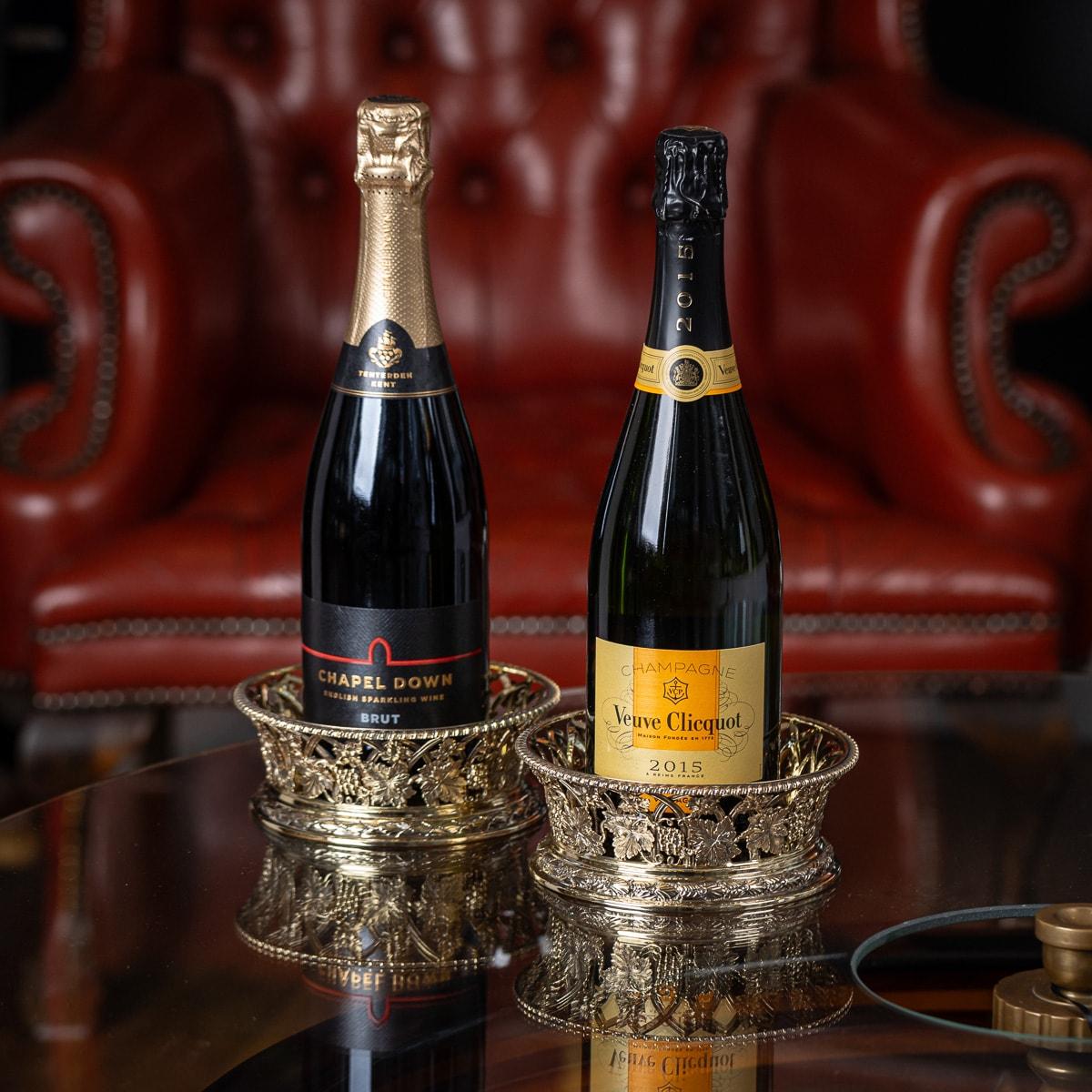 Antiguos posavasos de plata dorada maciza de principios del siglo XX para botellas de vino, de estilo Regencia, con un característico borde superior de cuerda y adornados con una serie de bandas entrelazadas, aplicadas con intrincados motivos de