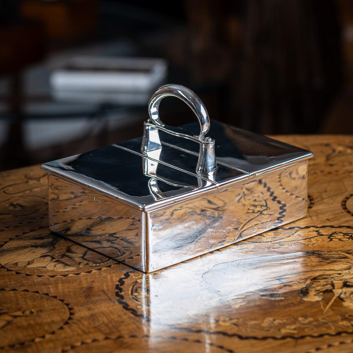 Antigua caja de puros de plata maciza eduardiana del siglo XX. Finamente elaborada, presenta un asa central curvada y dos tapas con bisagras, que se abren para revelar un compartimento dividido. El asa se levanta para activar un mecanismo interior,
