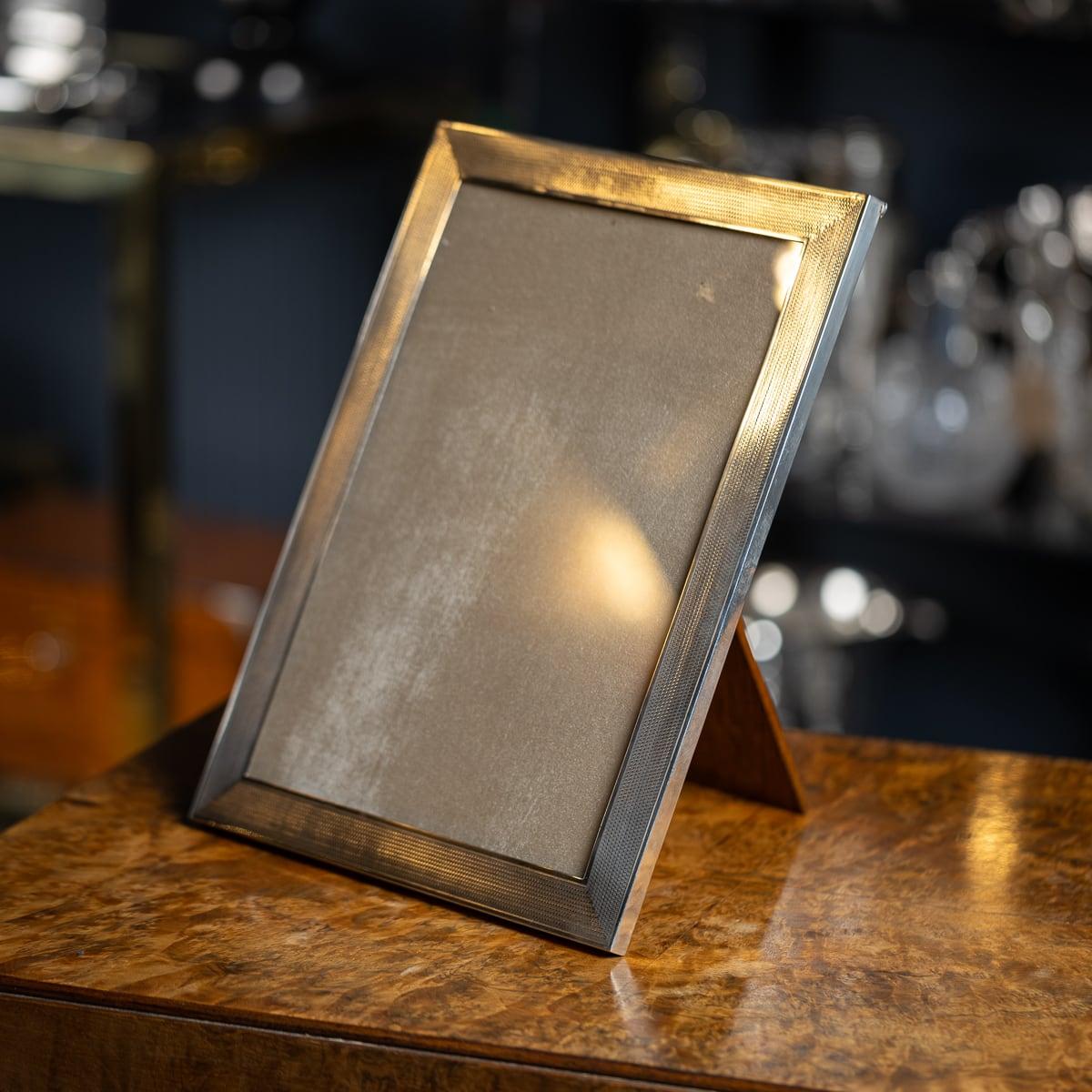 Antiguo marco de fotografía Art Decó inglés del siglo XX, de plata maciza, de forma rectangular con un diseño torneado a motor, cubierto tras un cristal y sobre un soporte de puntal de madera.

Plata inglesa con matasellos (norma 925), Birmingham,