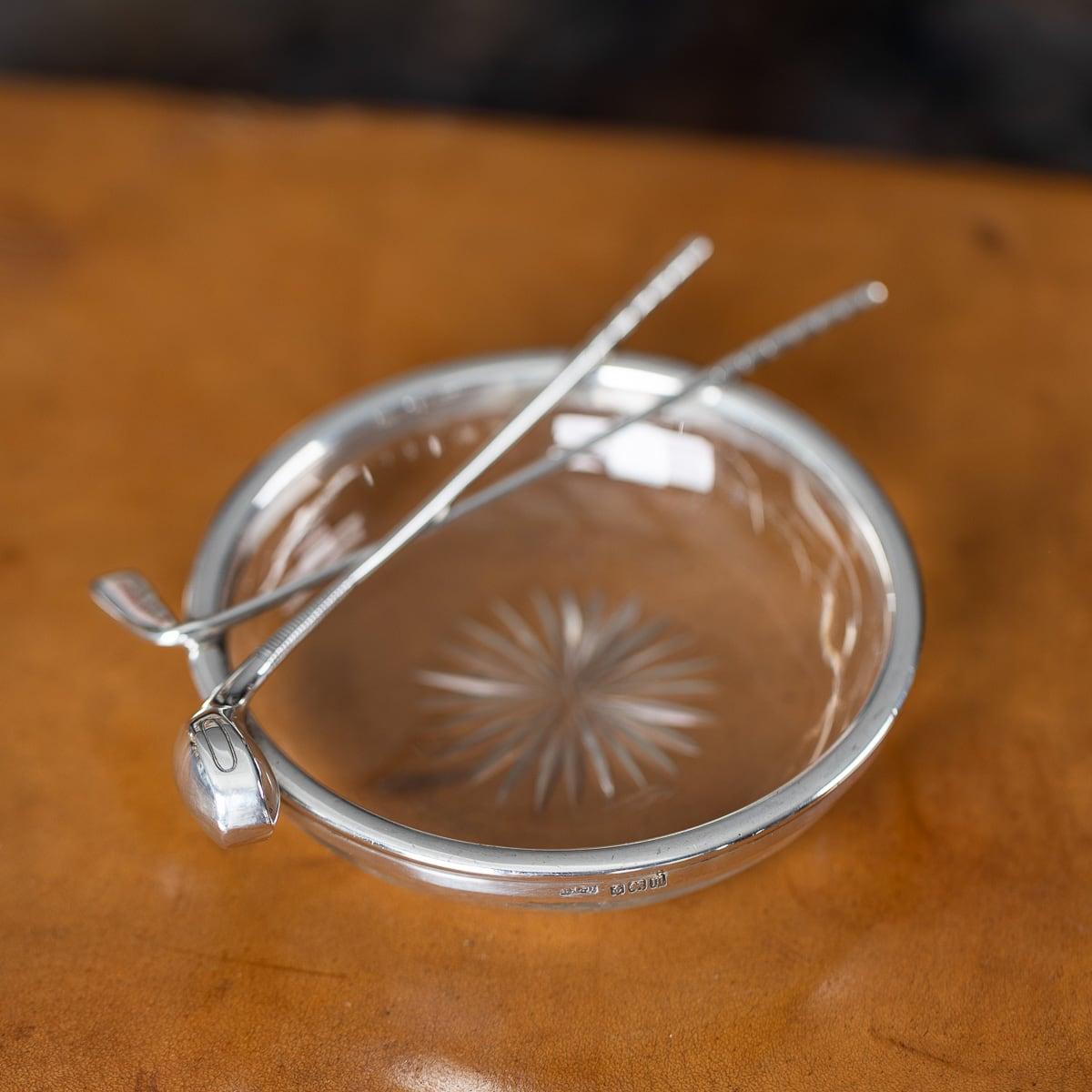 Antiguo cenicero inglés de plata maciza y cristal tallado de principios del siglo XX. El borde liso lleva dos palos de golf, que pueden utilizarse como reposa puros. El cenicero tiene un cuenco de cristal liso con una decoración central de cristal