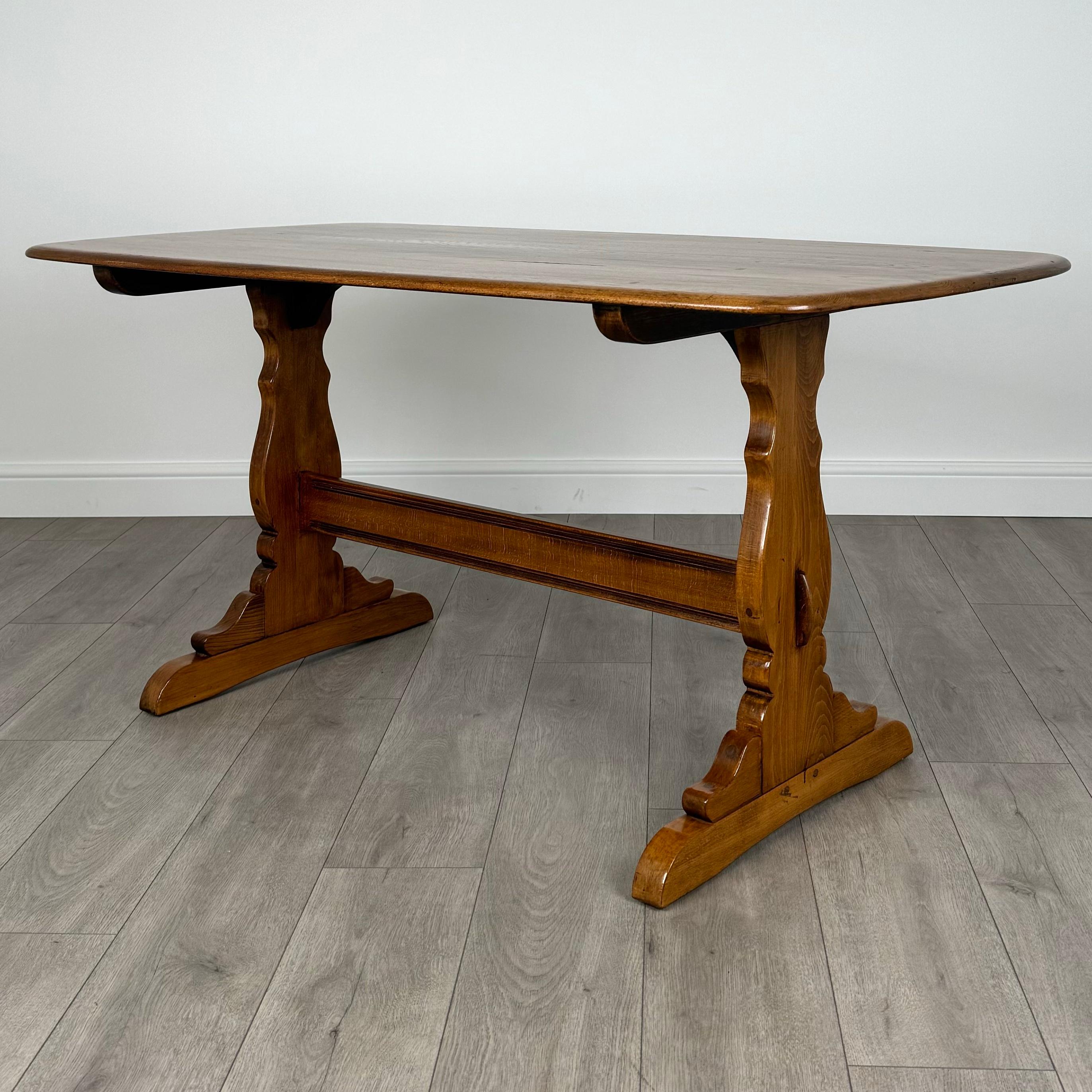 Cette table de salle à manger ancienne du XXe siècle, fabriquée par le célèbre Ercol, est un superbe exemple de qualité d'exécution et de design intemporel. 
Fabriquée en orme, la table est dotée d'un piètement classique de style réfractaire qui lui