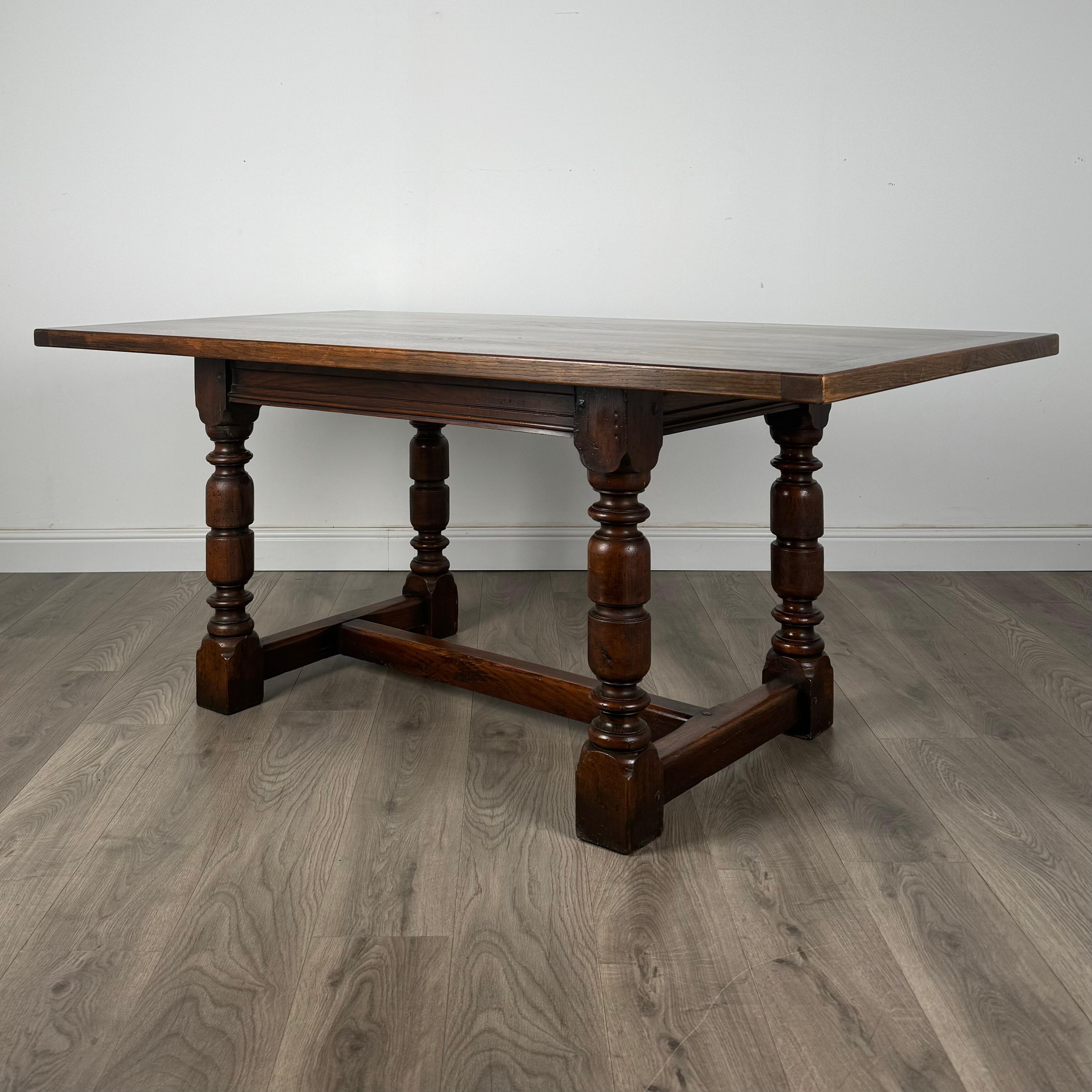 An antique 20th-century dining table crafted from solid oak, offering exceptional quality and timeless elegance. The table features a substantial overhang on both ends for added comfort and a refined look. It stands on turned legs with a cross