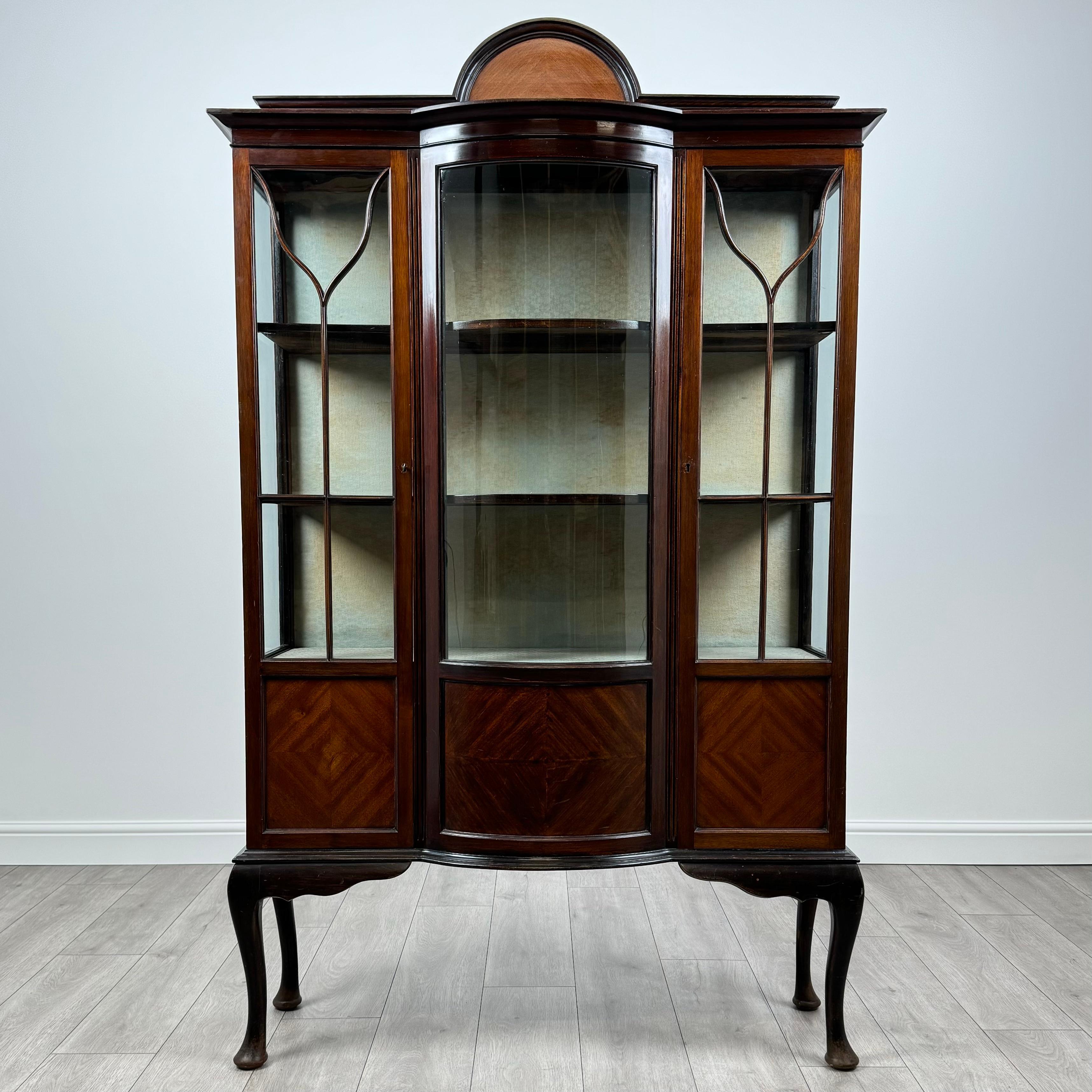 This stunning antique 20th century display cabinet is crafted from rich mahogany, offering both elegance and practicality. 
Standing on decorative cabriole legs, it features a beautifully glazed front and sides, allowing a clear view of the