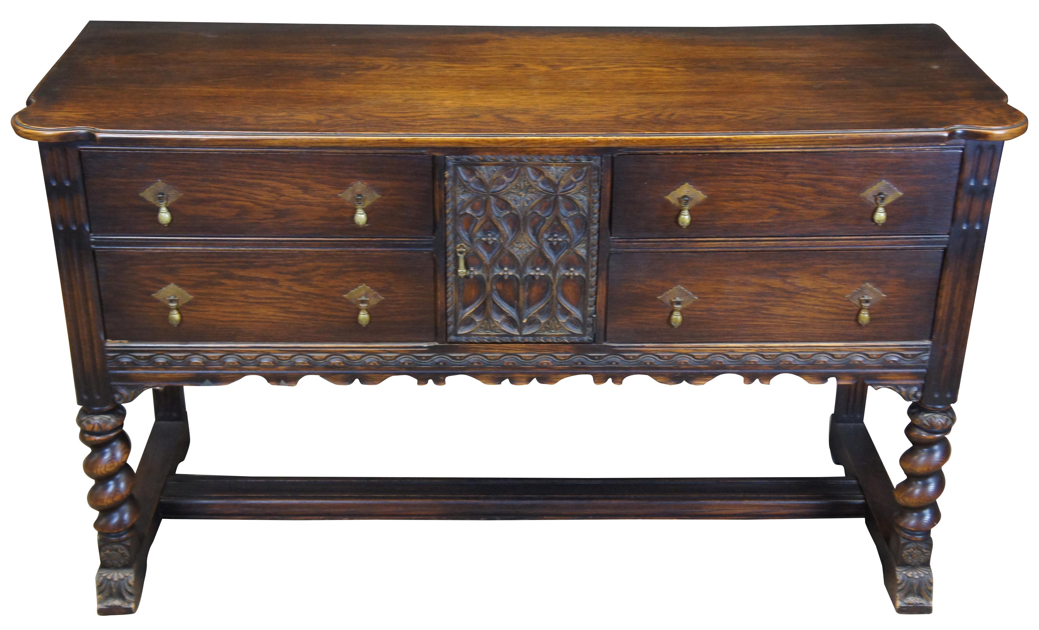Early 20th century Spanish Revival buffet. Made from oak with intricately carved details. Barley twist legs and trestle base. Features four drawers and center cabinet with brass hardware.
 