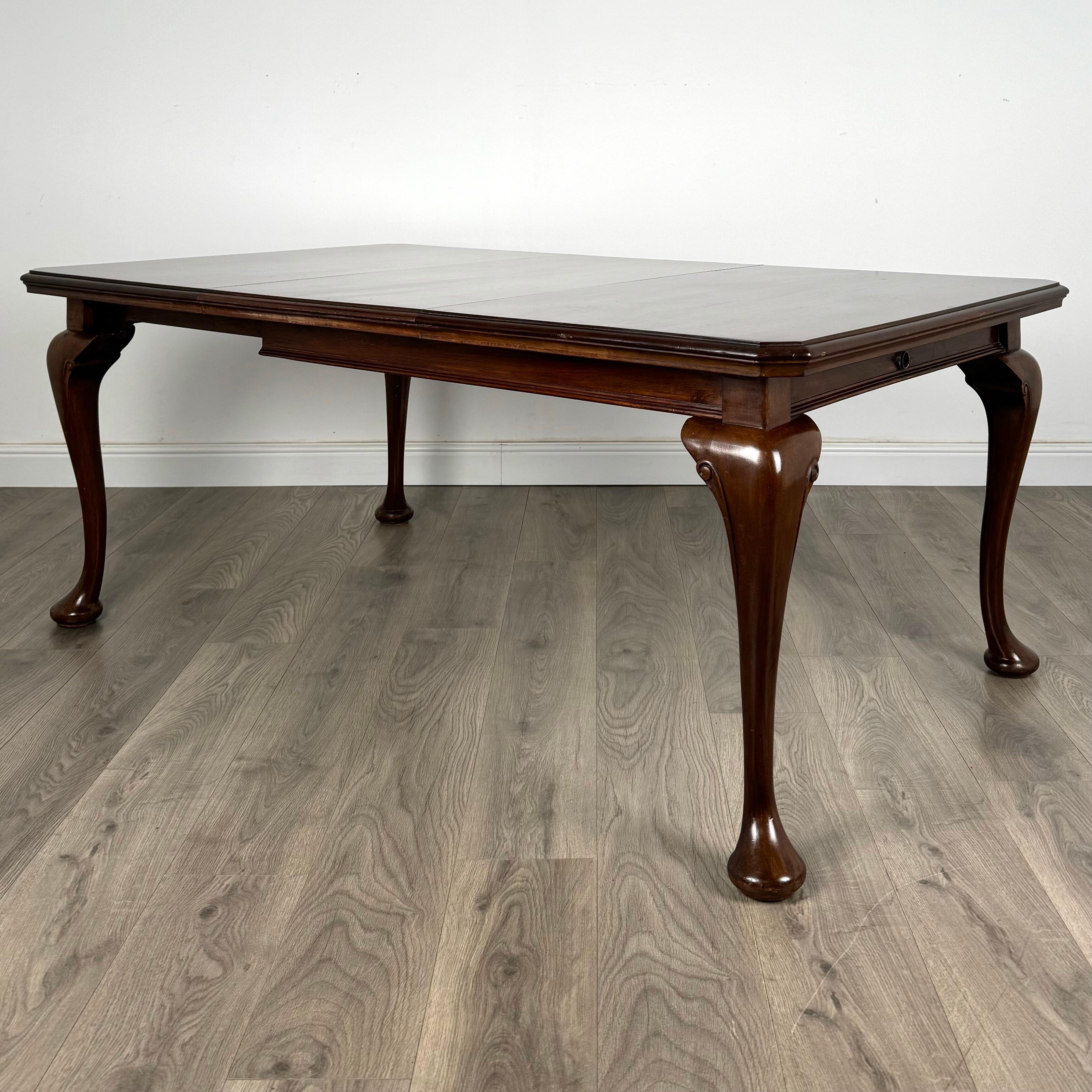 This exceptional 20th-century dining table, crafted from mahogany, embodies the elegance and sophistication of the Queen Anne style. Featuring beautifully curved cabriole legs, the table exudes a timeless charm and classic grace. The rich mahogany