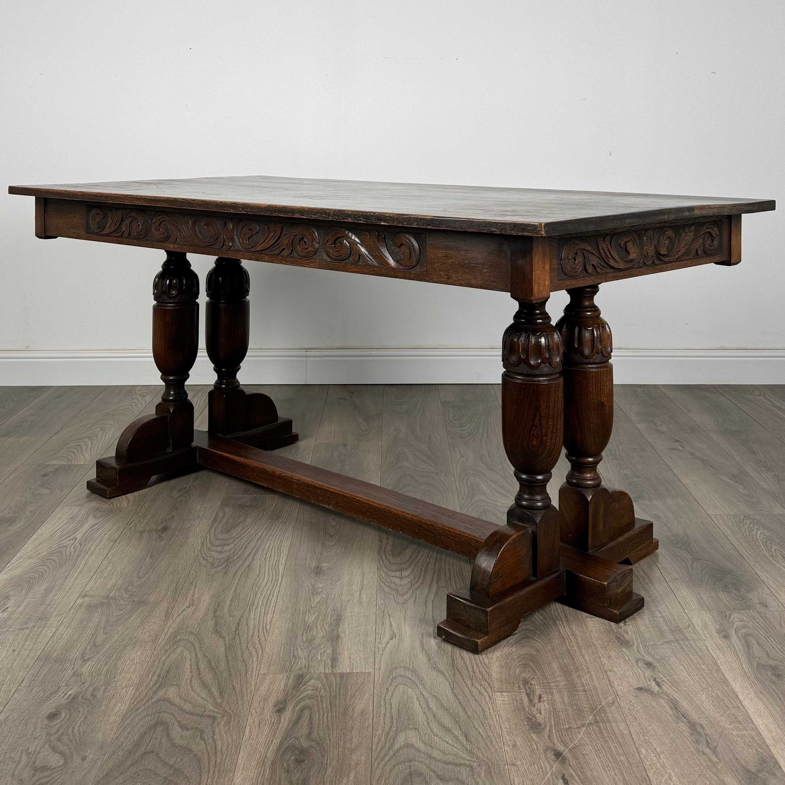 Une élégante table de salle à manger ancienne du 20e siècle, fabriquée en chêne avec une base de style réfractaire caractéristique. La table présente une frise magnifiquement sculptée et met en valeur un grain et une couleur riches et étonnants. Le