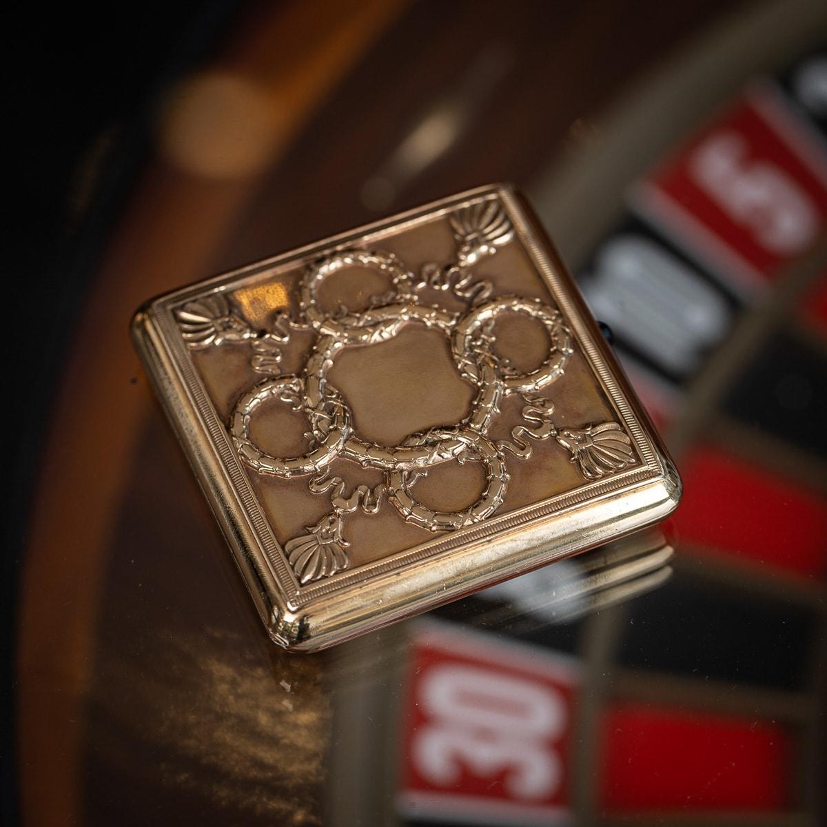 Antique early-20th Century Russian Faberge silver gilt cigarette case, The lid features a design of interlocking laurel wreaths and ribbons suspending tassels. The push piece is set with a cabochon sapphire and opens to reveal a plain