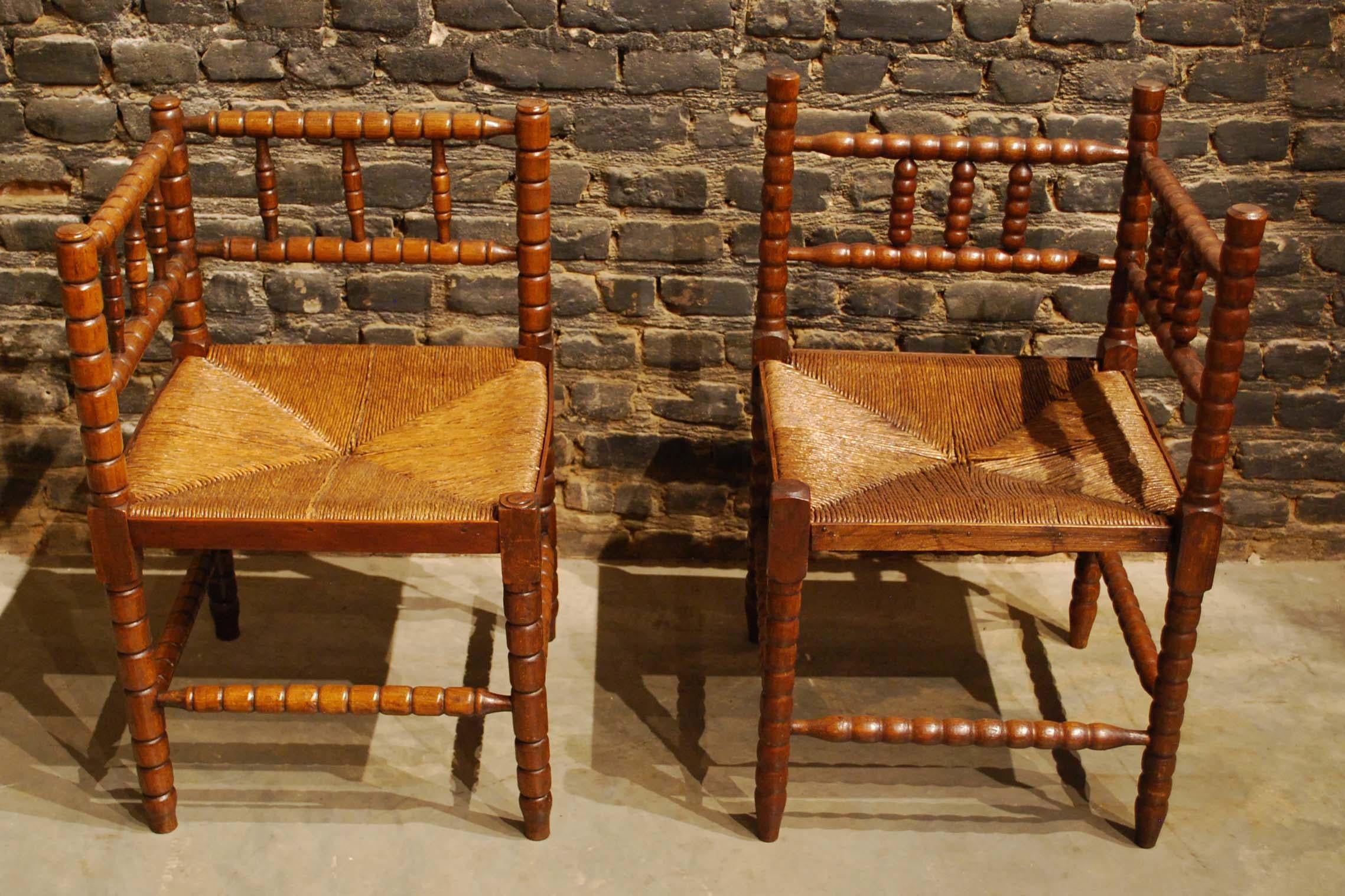 A beautiful seating arrangement of two corner chairs. 
The chairs were made in solid beechwood with original rush seats. This rustic set of antique double railed chairs with Classic bobbin turned legs and cross supports are slightly different.