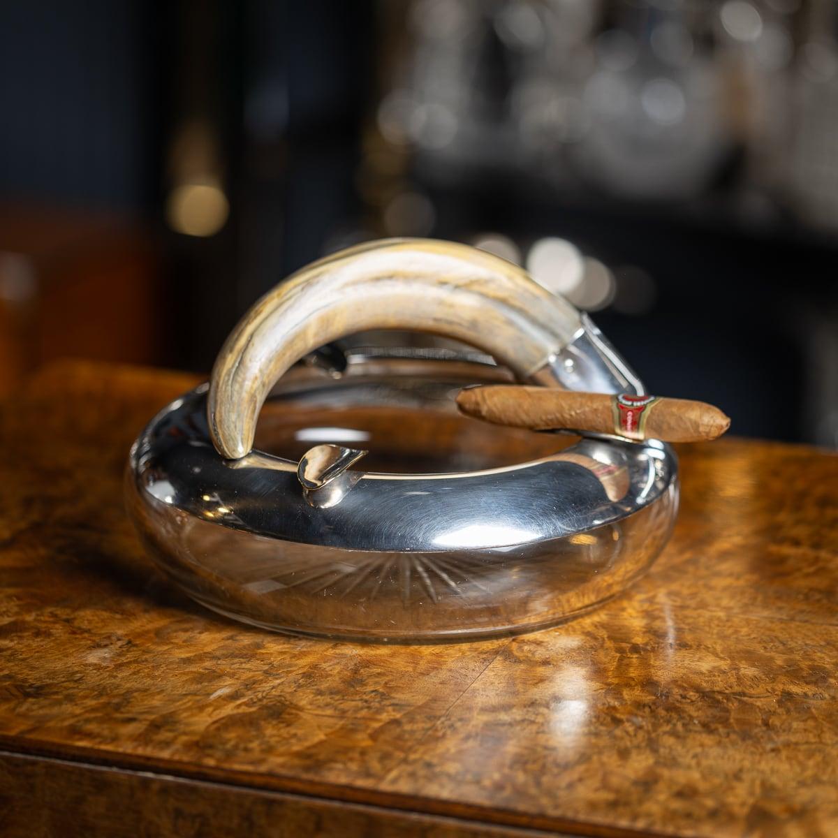Antique early 20th Century British silver plate & cut glass mounted cigar ashtray. The plain rim applied with three cigar rests. Mounted to the rim, a boars tooth adds a decorative touch. Marked 