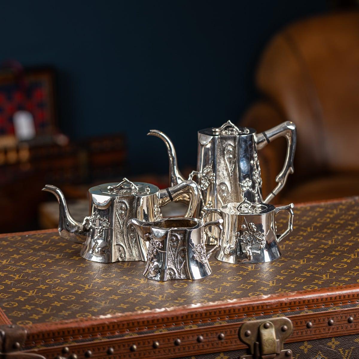 Service à thé ancien en argent massif d'exportation chinoise du début du 20e siècle, comprenant une cafetière, une théière, un sucrier et un pot à lait, chaque corps en forme de tronc d'arbre appliqué de fleurs de prunus et de décorations en relief,