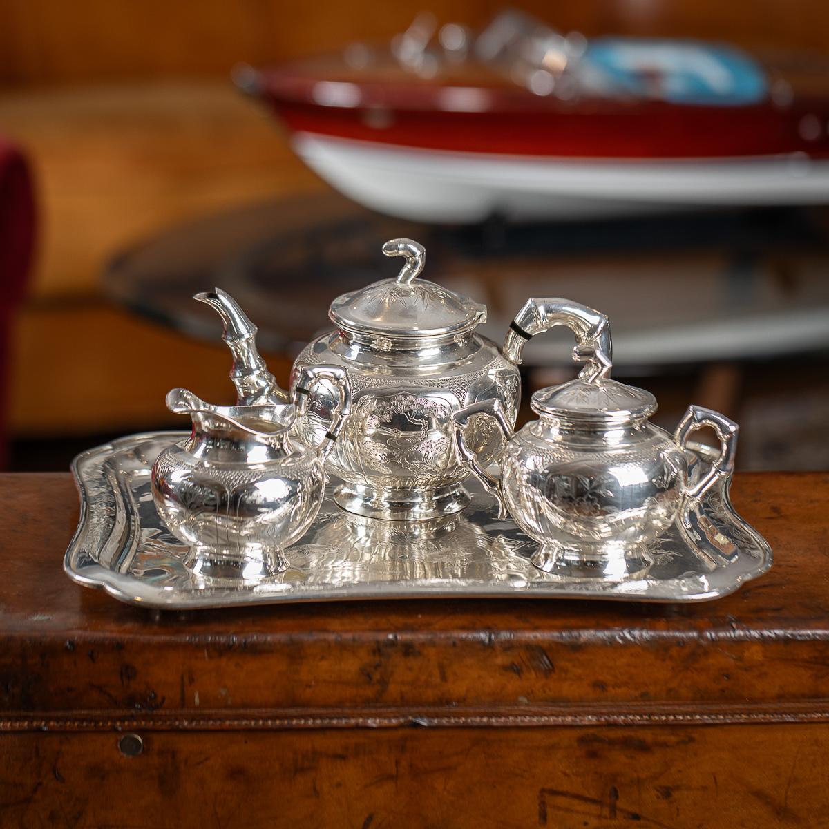 Antiguo y raro servicio de té en bandeja de plata maciza china de principios del siglo XX, compuesto por tetera, azucarero con tapa, lechera y bandeja. Cada cuerpo está grabado a mano con aves exóticas dentro de estilizadas cartelas, las asas huecas