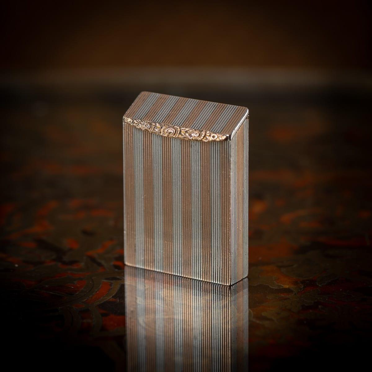 Antico porta-fiammiferi inglese del XX secolo in argento massiccio e oro 9 carati con percussore. Il pezzo presenta un corpo finemente strutturato e ornato da strisce d'oro e d'argento alternate. Il coperchio è dotato di una punta di pollice