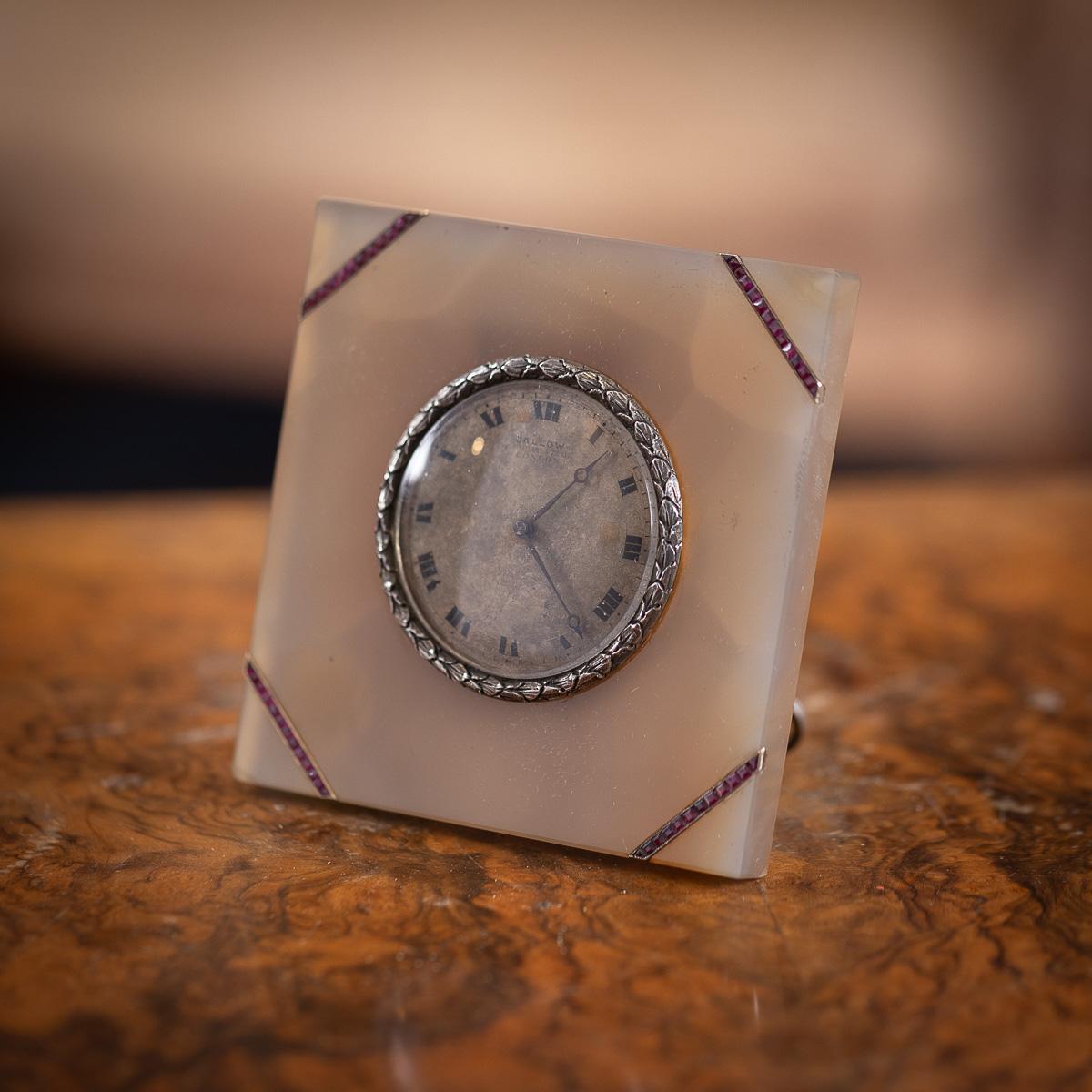 Antique early-20th Century Edwardian travel clock featuring a solid silver inset clock with ruby mounted decorations on translucent agate body. The clock has a signed easel on the back and is in working order. Included, the original retailers silk